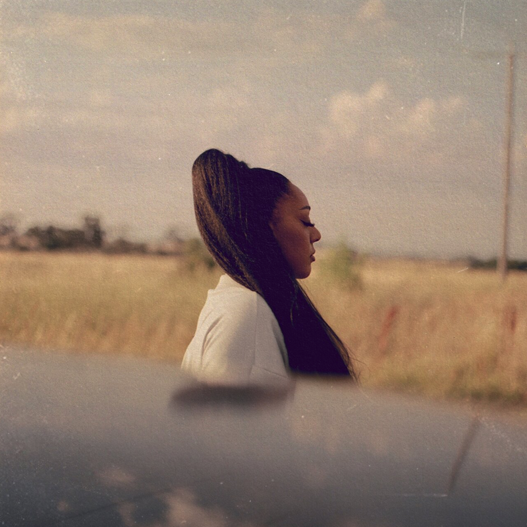 A woman with long braided hair and a white top standing in a field with her eyes closed, side profile, on a sunny day. Soli, Temporary Low