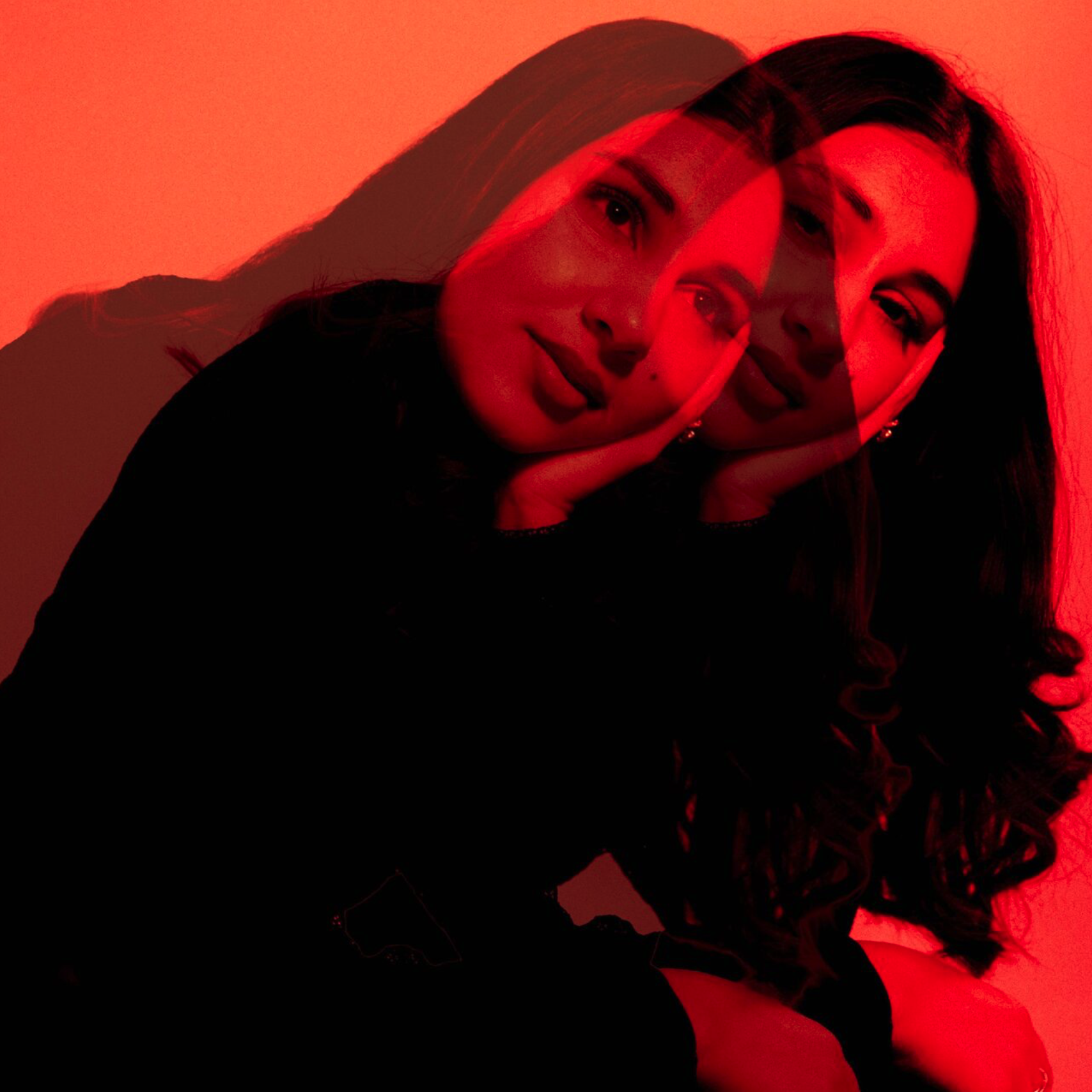 A woman with dark hair, resting her face on her hand, with multiple red-tinted overlapping images creating a layered effect, against a red background. Zuhair