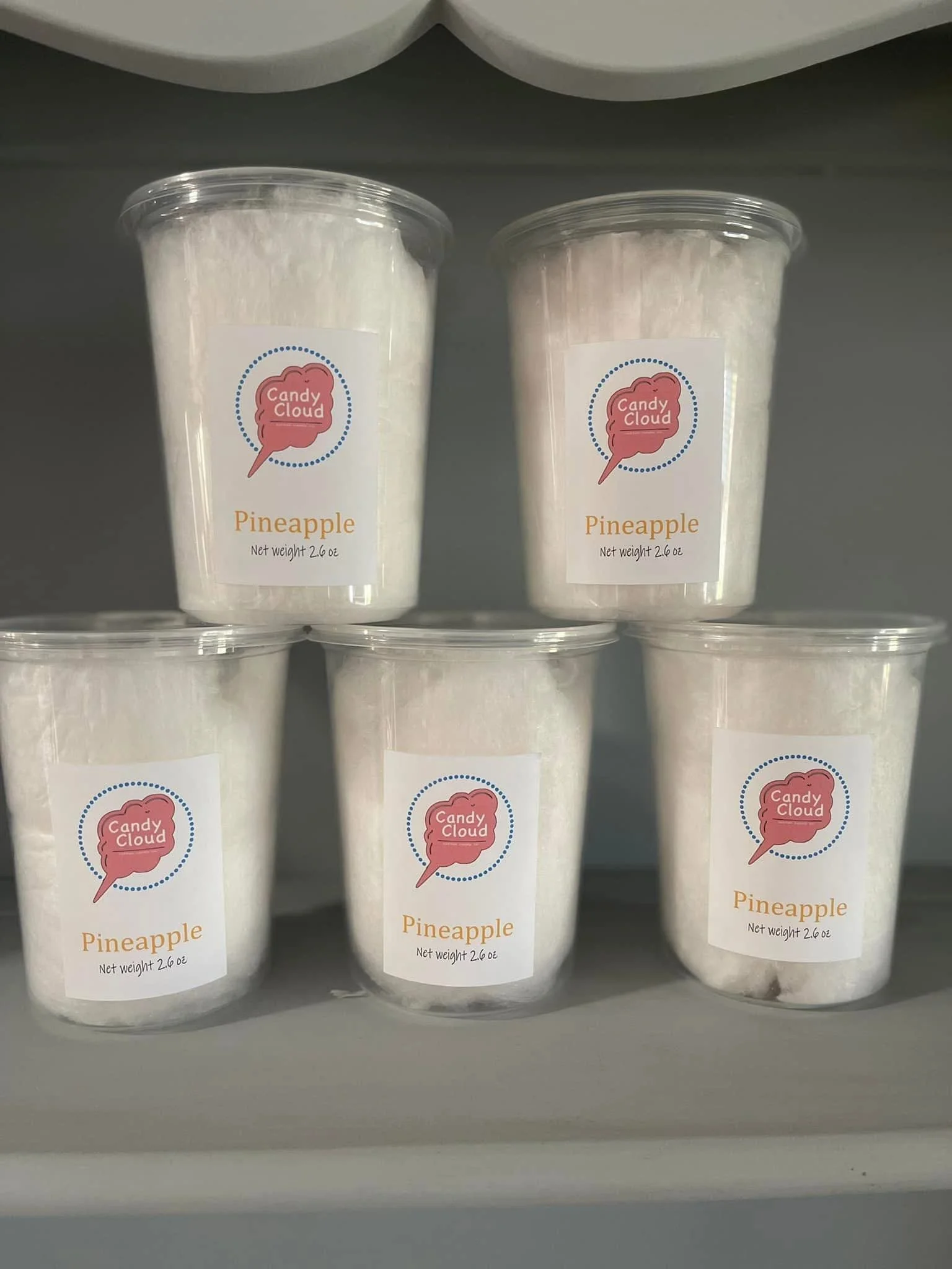 Five containers of Pineapple flavored snow or ice treats labeled 'Candy Cloud'. The containers are clear plastic with white snow-like contents and have labels with a pink candy cloud graphic and the words 'Candy Cloud' and 'Pineapple'.