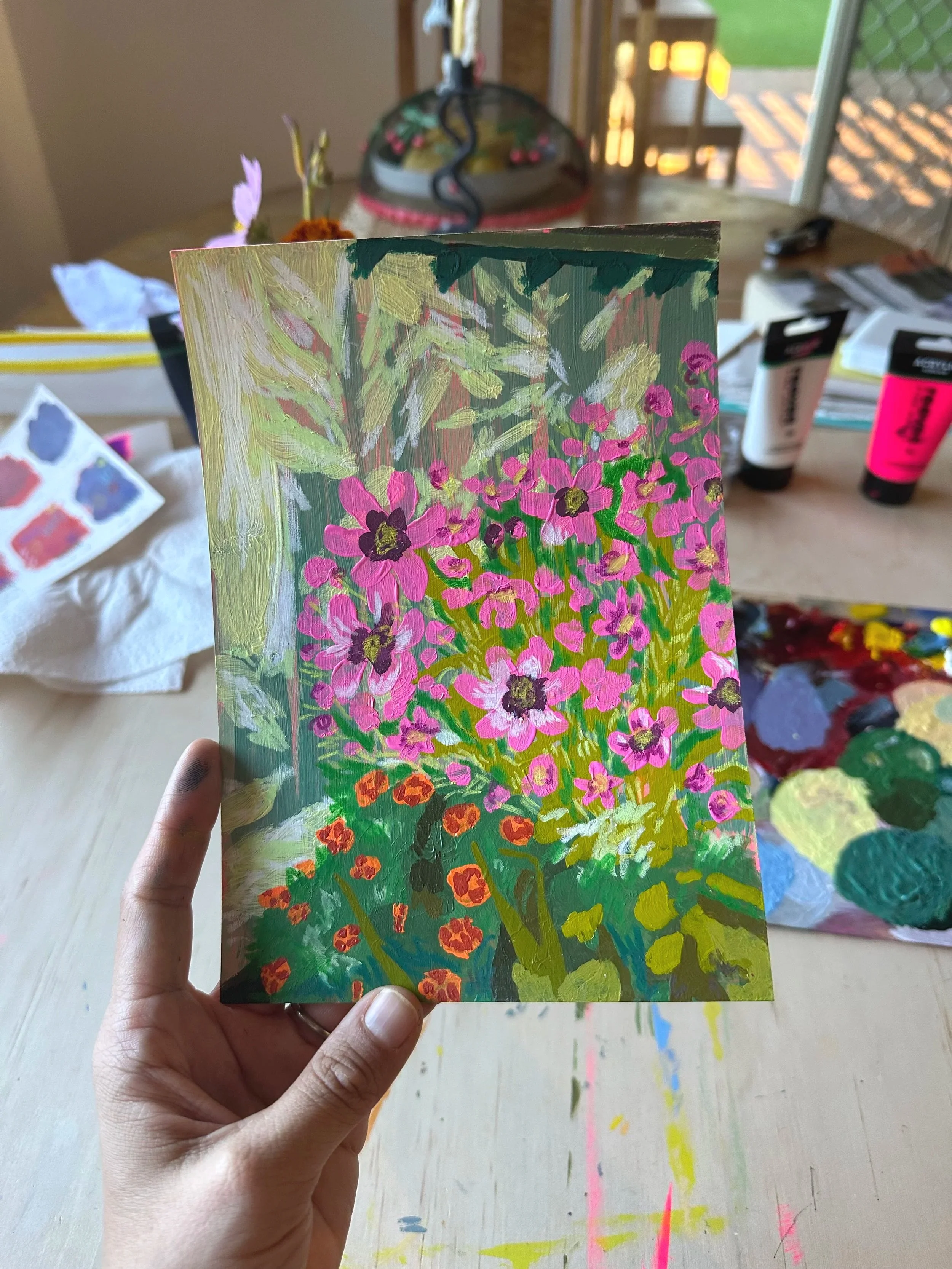 Photo of a painted artwork depicting pink flowers. The painting is being held up to the camera by a hand.