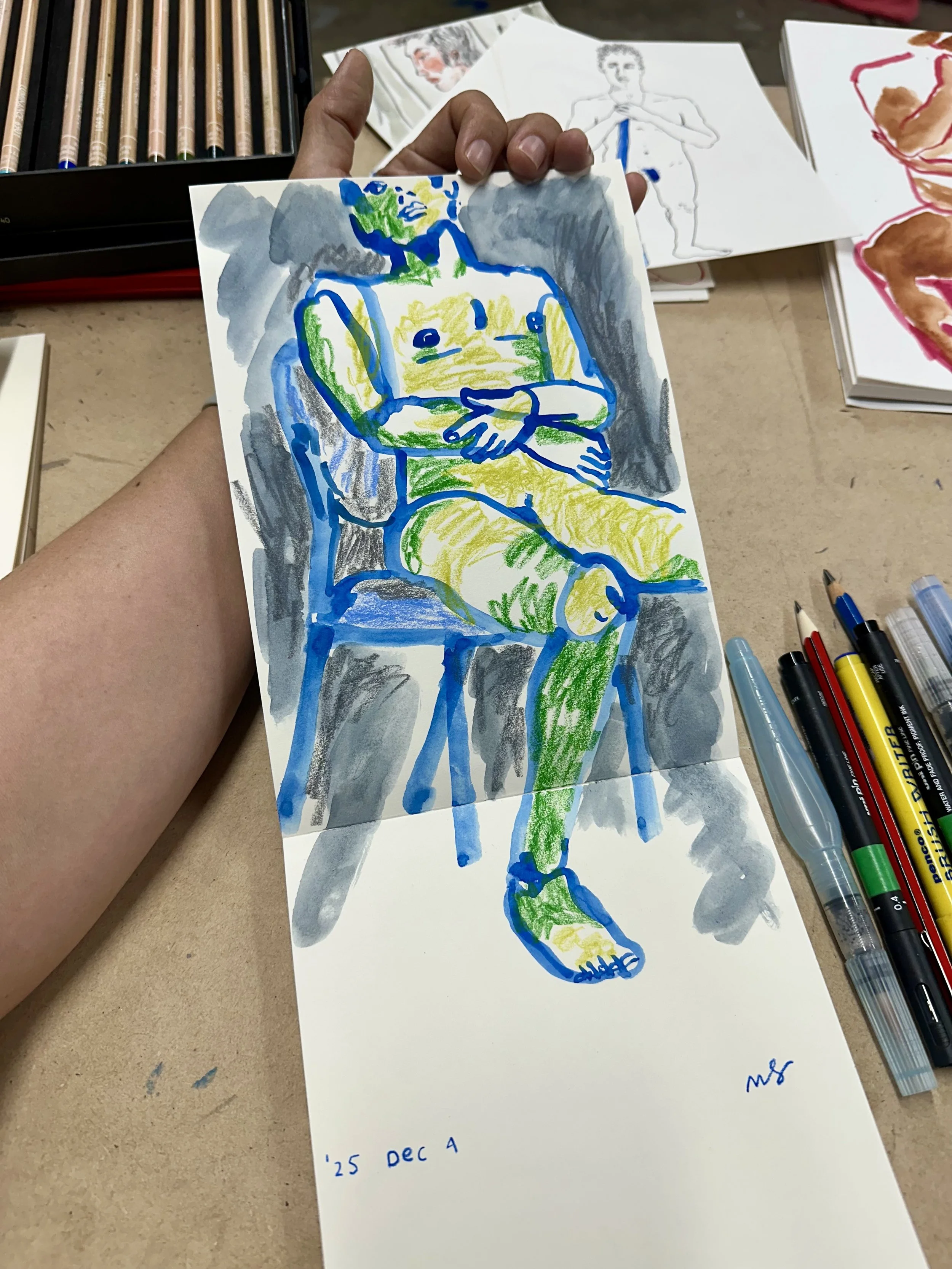 Photograph of a painted figure in blue and green, placed in a sketchbook.
