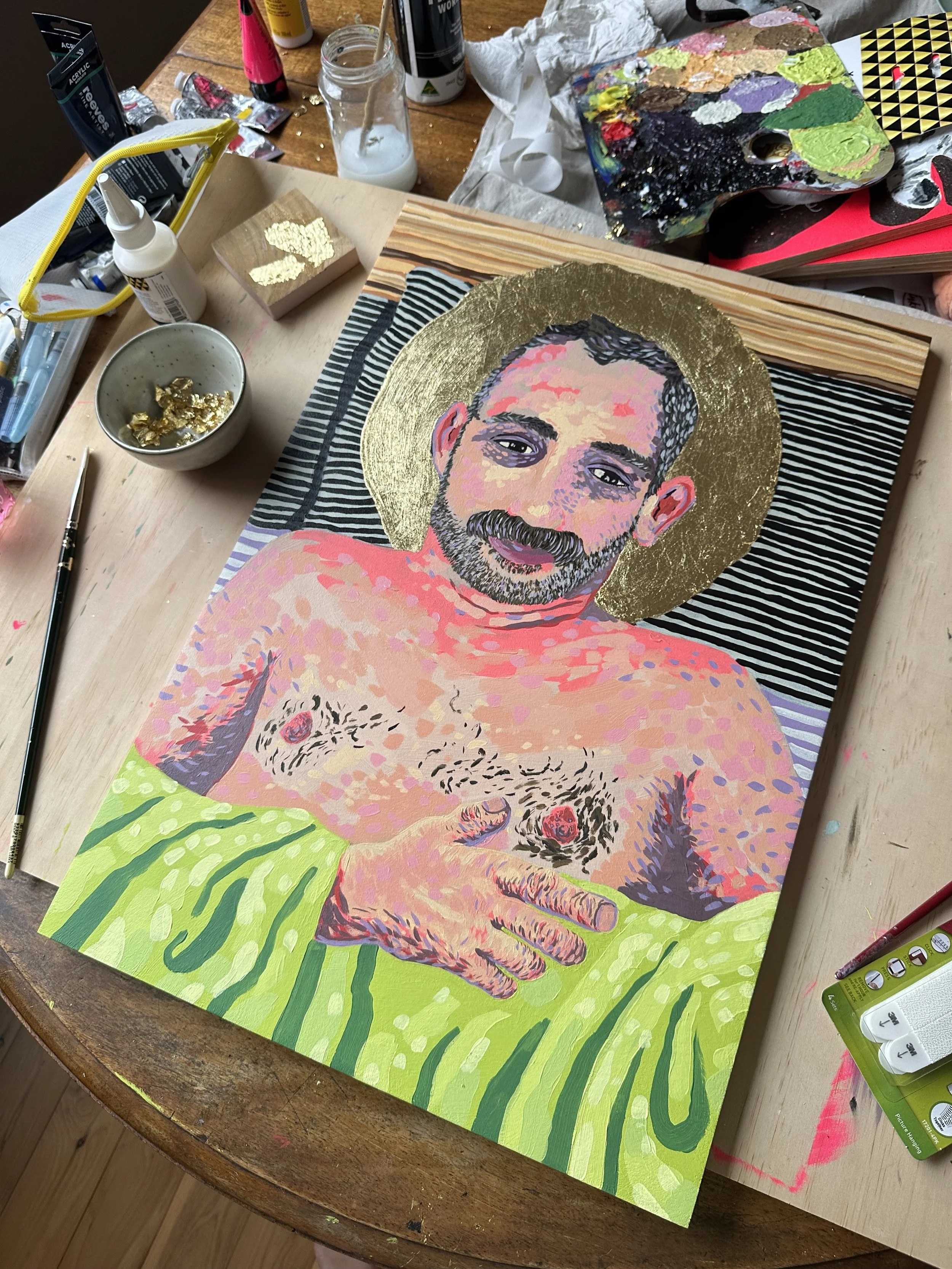 Photo of a painted portrait atop a table. The figure in the portrait has a gold 'halo' and is holding a bright green sheet with one hand.
