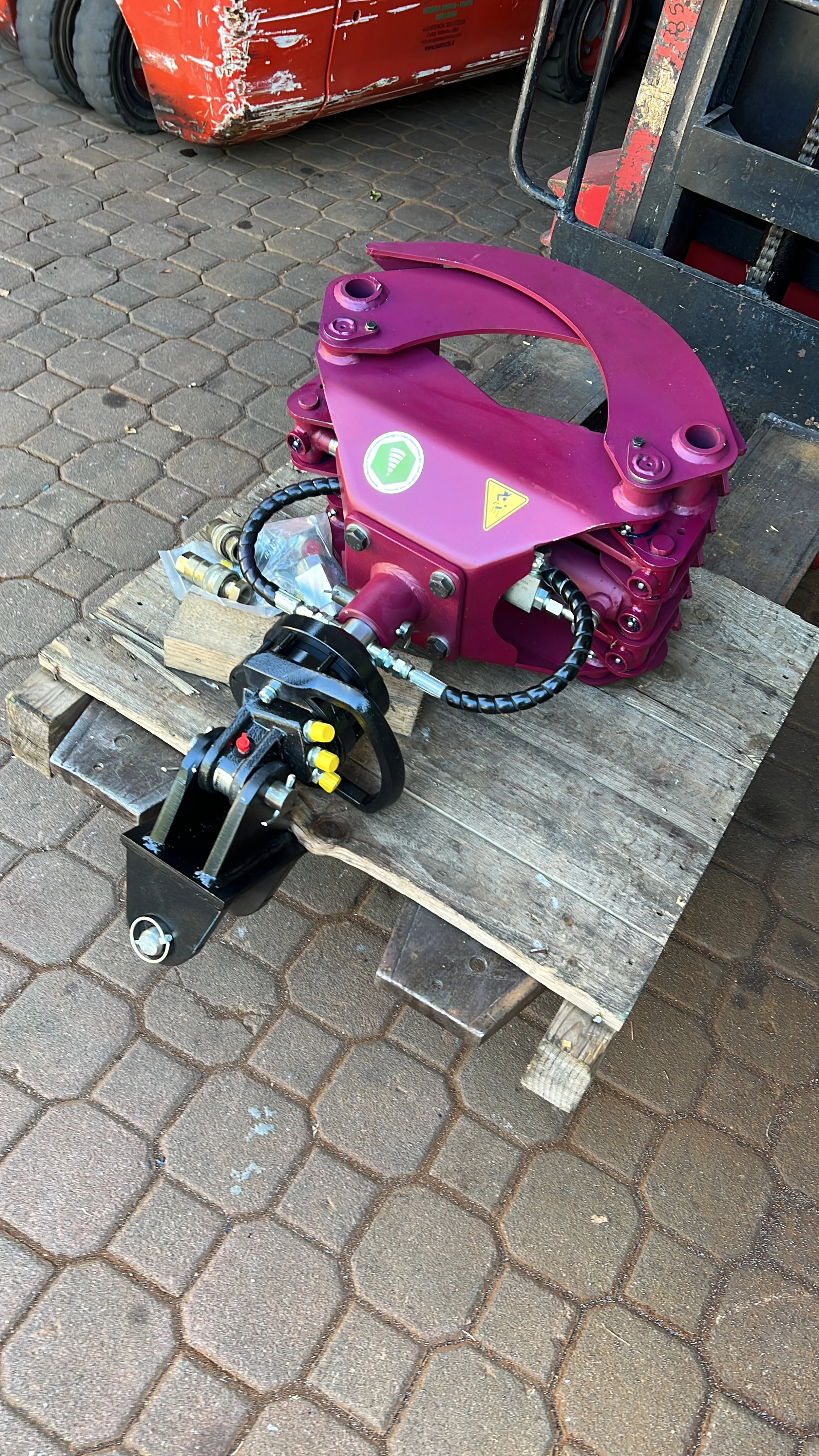 Pinza forestale con rotatore e forcella a bascula pronta per la spedizione, appoggiata su bancale EUR in officina