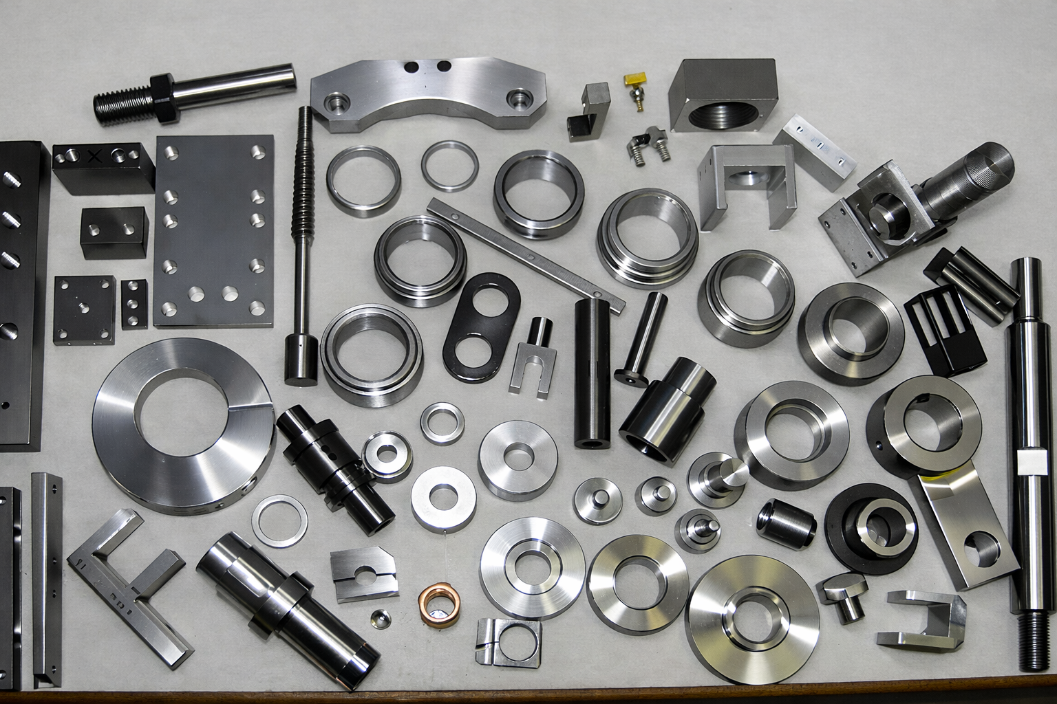 Parti metallici di diverse forme e dimensioni disposti su un tavolo, probabilmente componenti di macchinari o strumenti industriali.