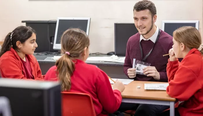 Teacher showing photograph to three students in a classroom setting with computers in the background.