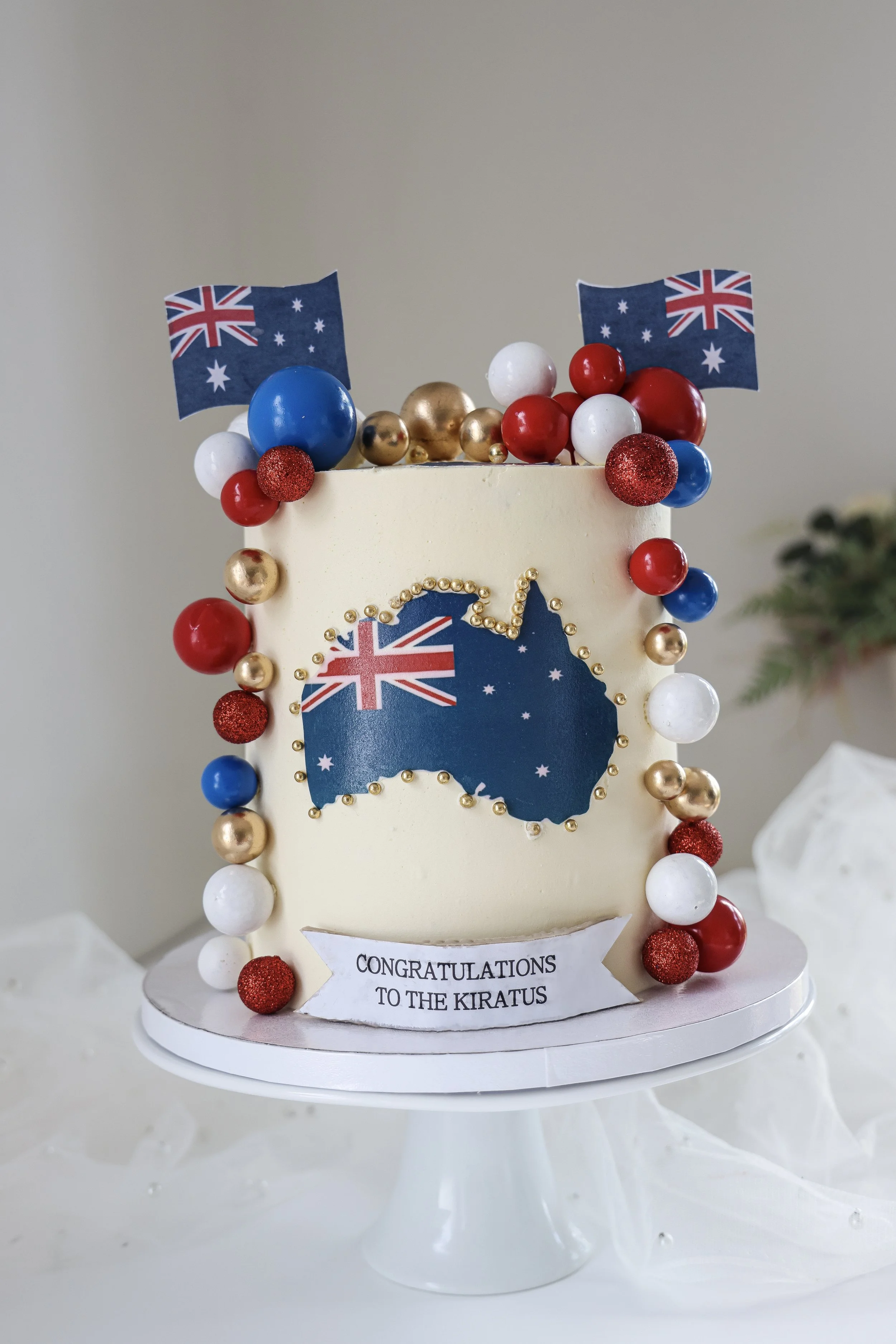 Celebration cake decorated with Australian flags, gold, red, white, and blue balls, and a sign that reads 'Congratulations to the Kiratus.'