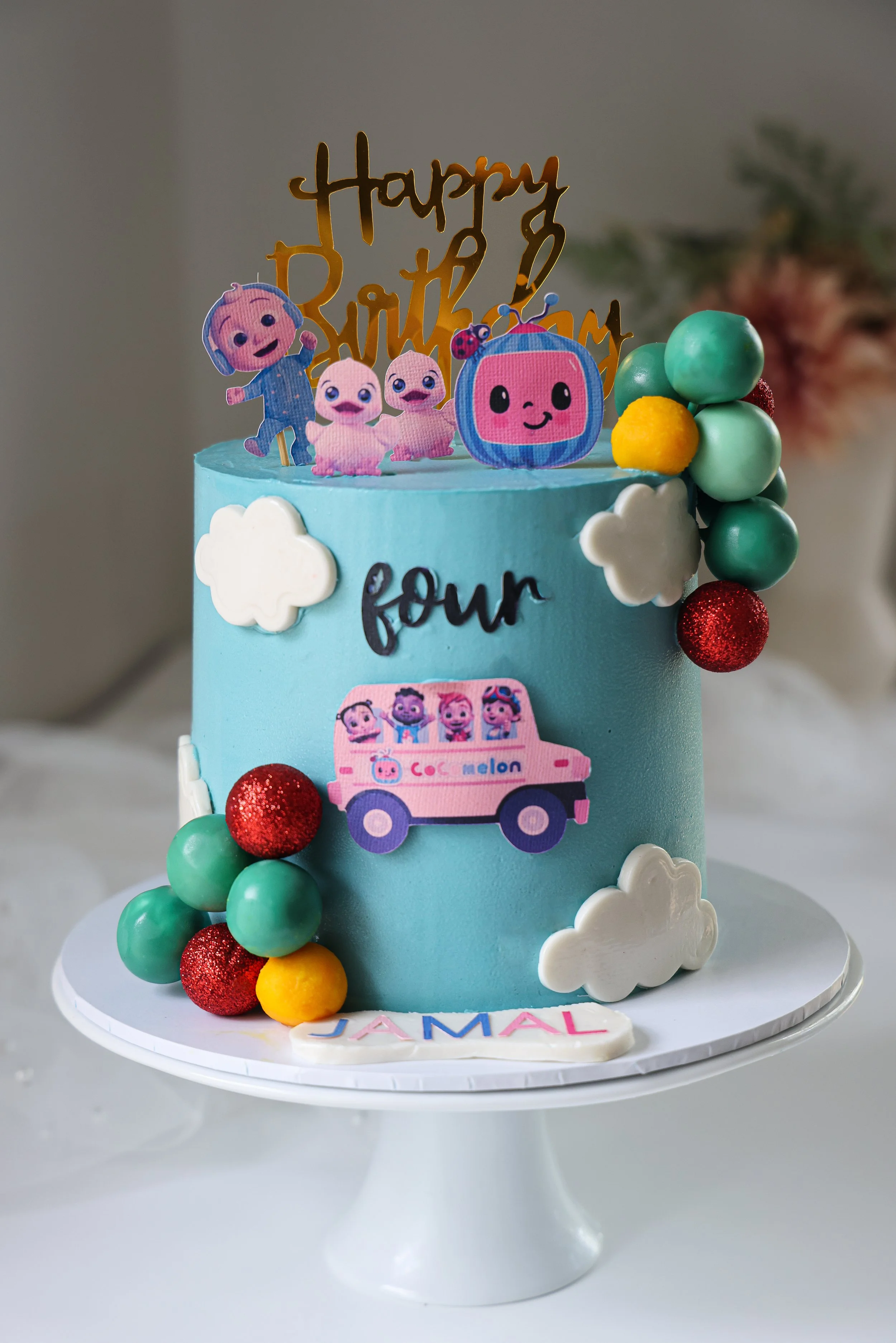 A colorful Cocomelon birthday cake decorated with cartoon characters, clouds, and balls, celebrating a kid's birthday.