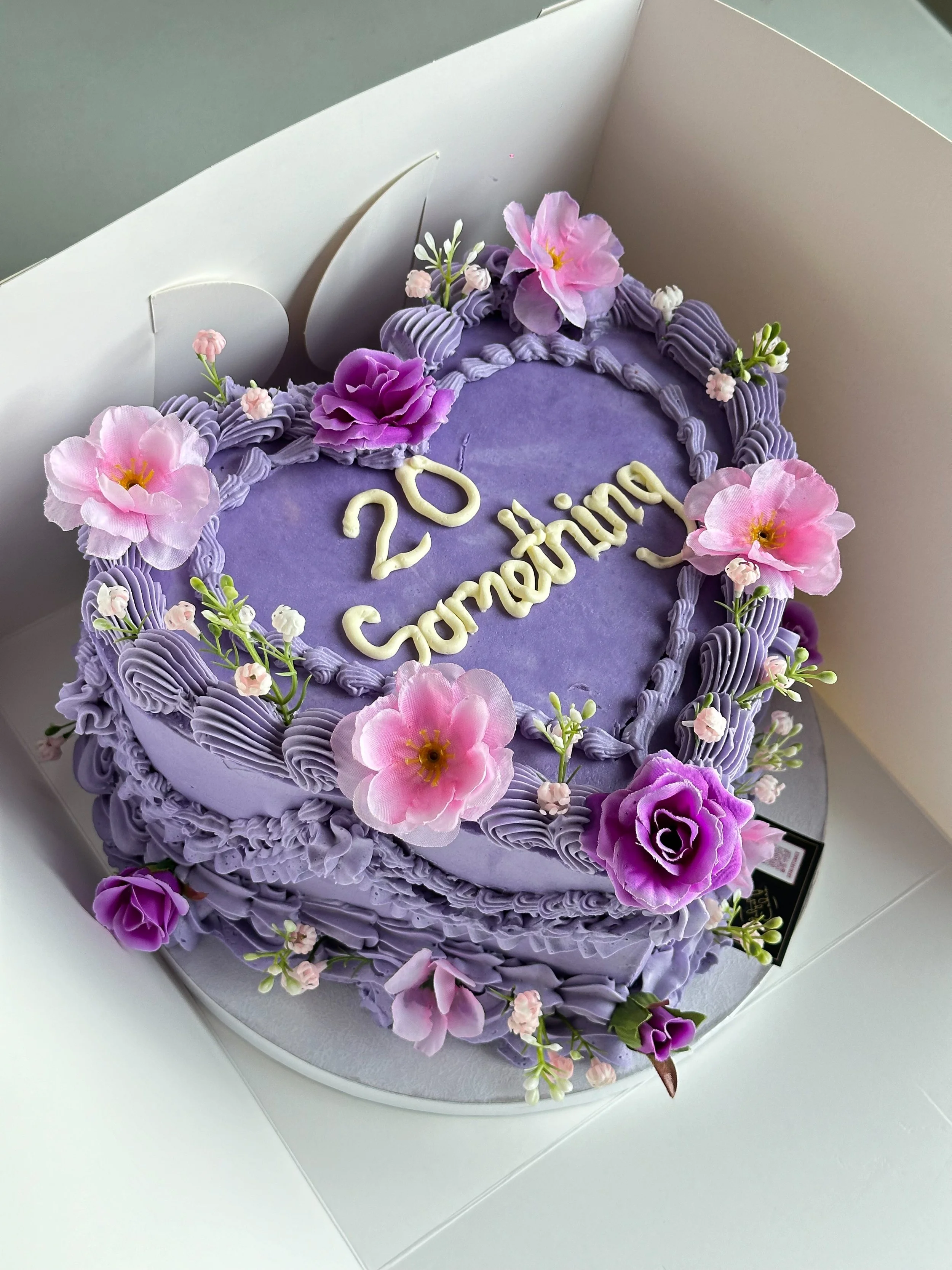 A purple vintage heart-shaped cake decorated with pink and purple flowers. This is a trendy cake and is cute and lovely.