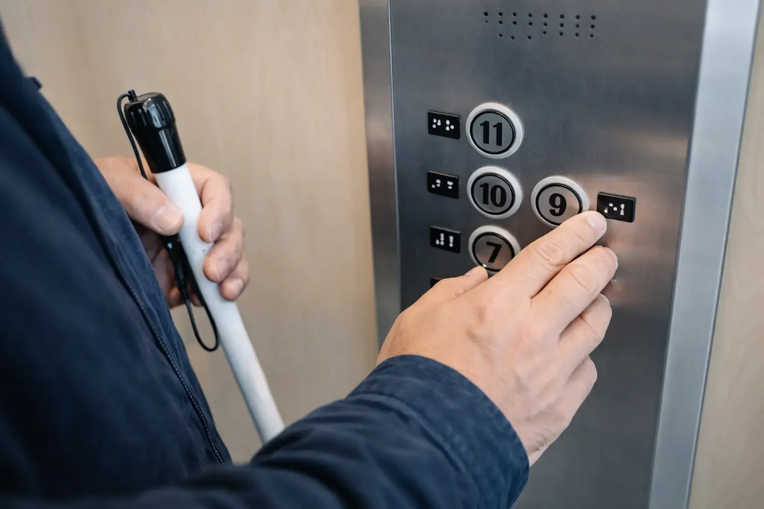 Person pressing the '9' button in an elevator keypad while holding a white pointer in their left hand.