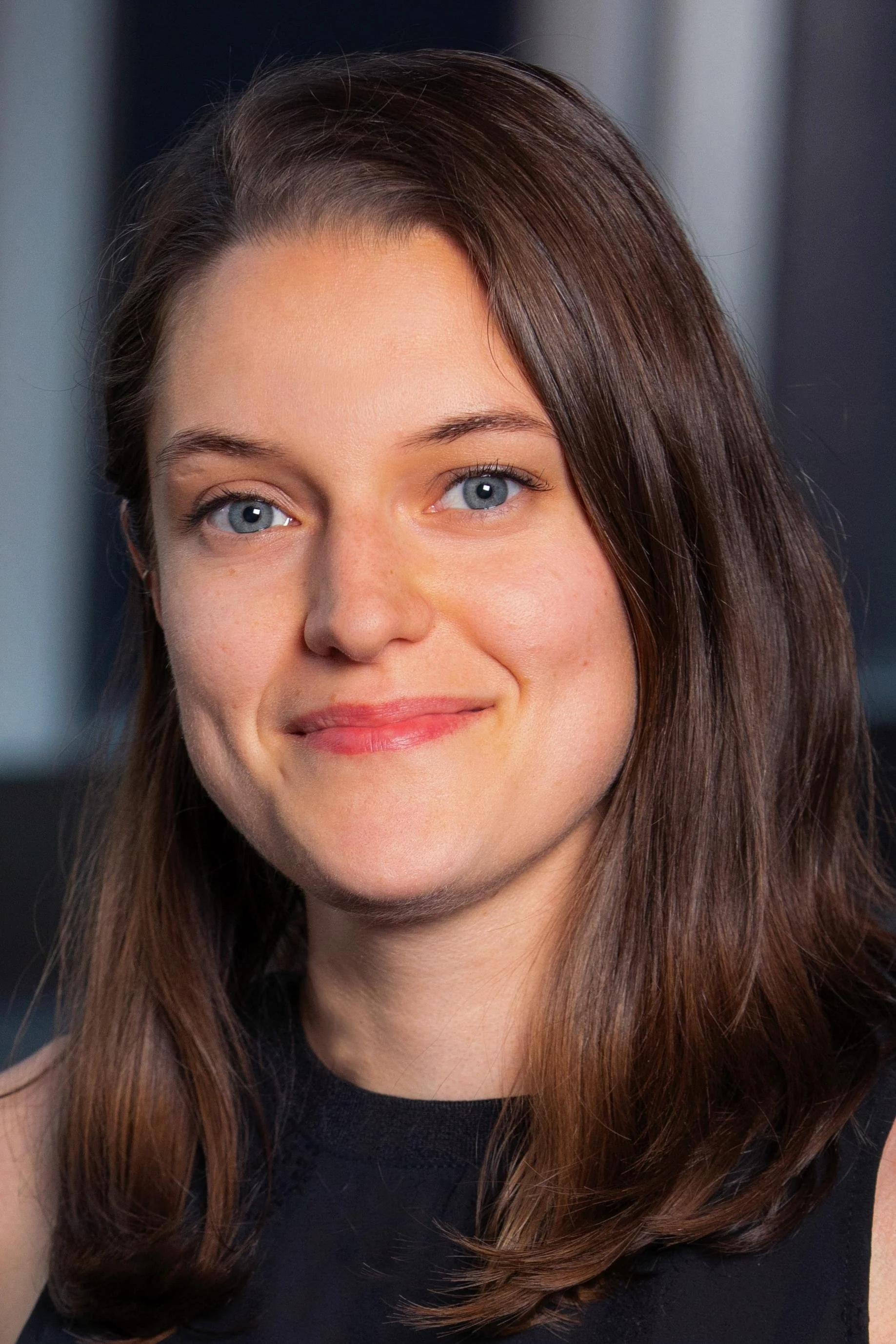 Dr. Evelina Pituch, straight brown hair, blue eyes, and a light complexion, smiling gently, wearing a black top, against a dark background.
