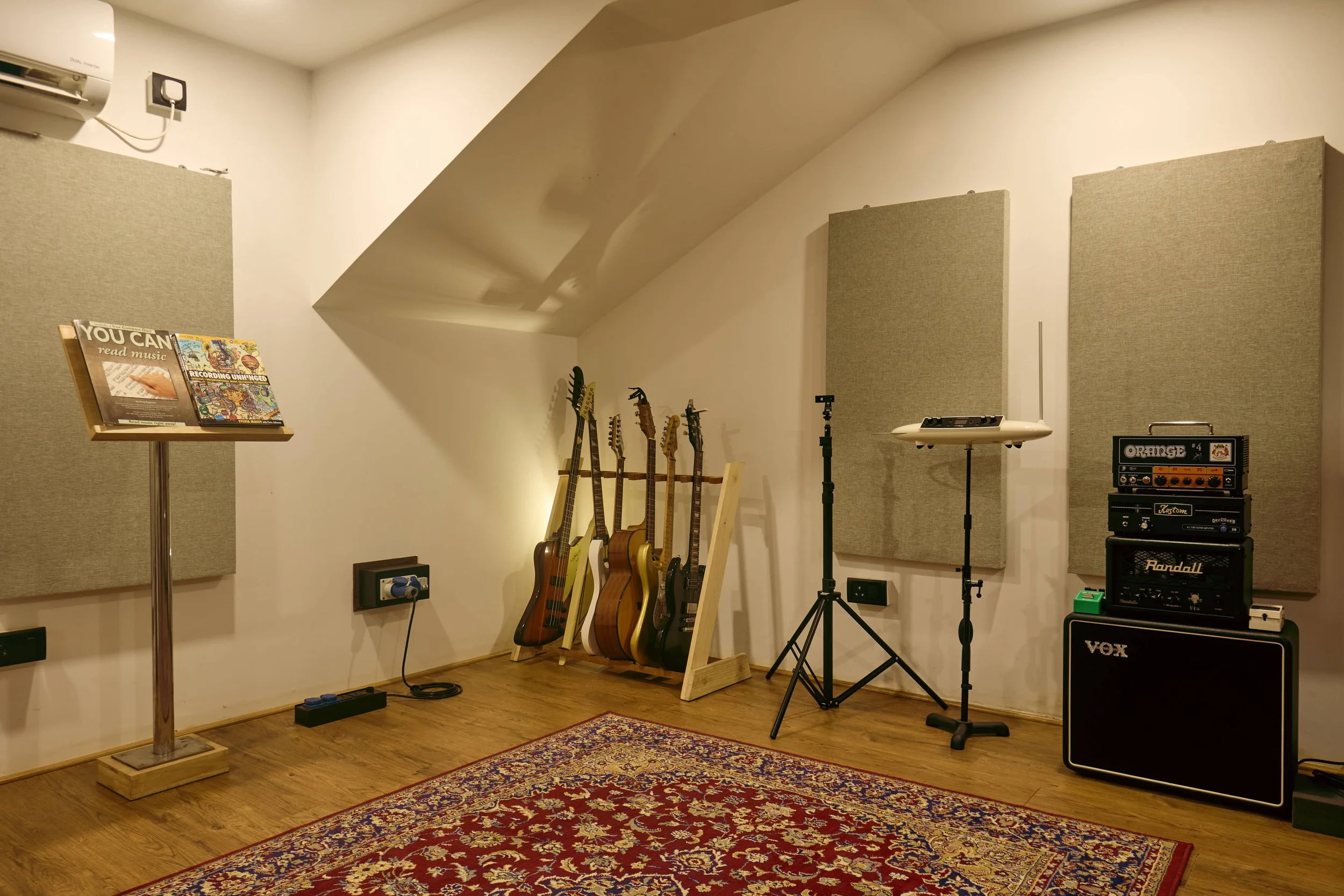 Music studio with guitars, amplifiers, microphone stands, and acoustic panels on the wall.