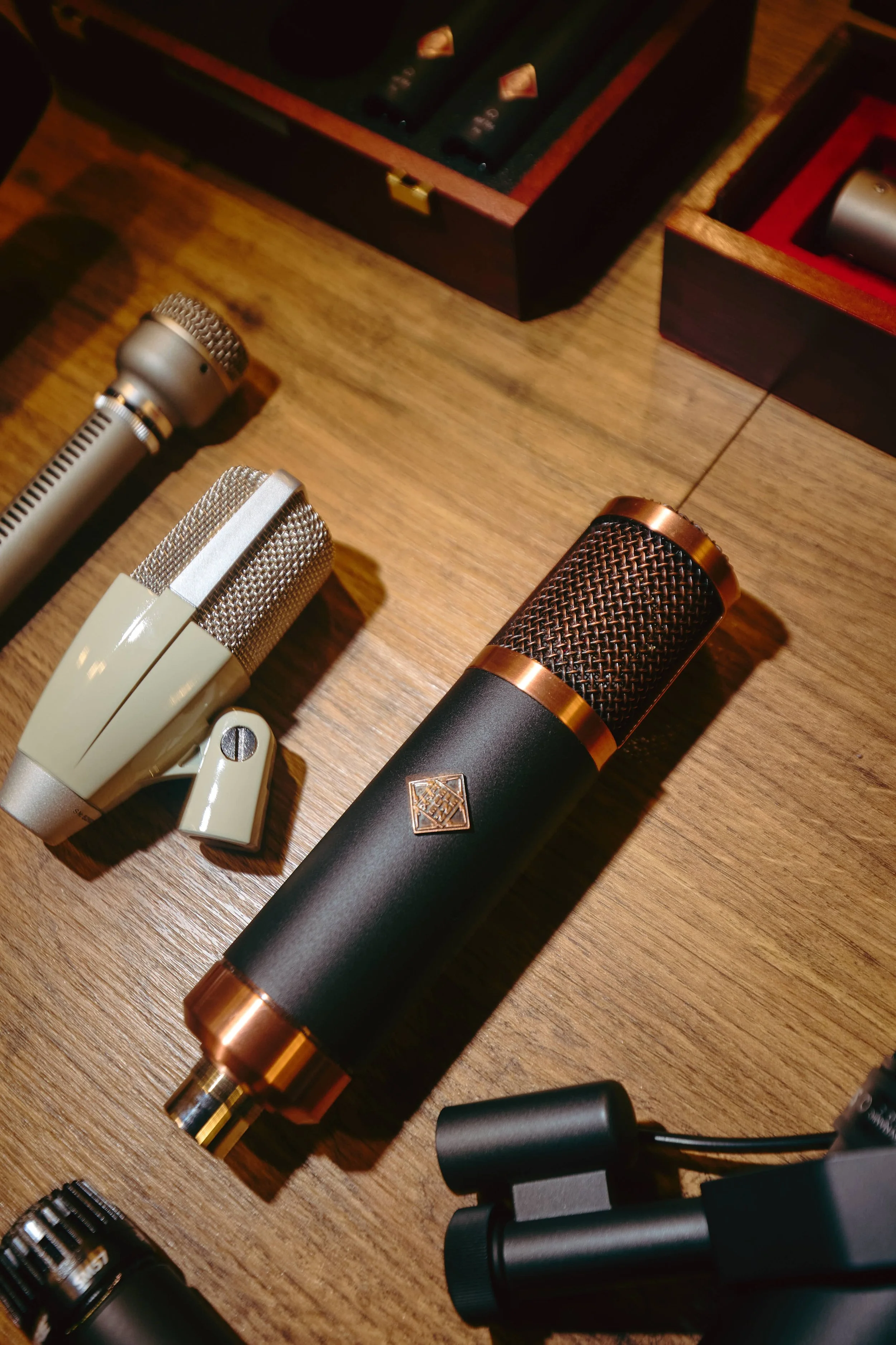 A collection of vintage microphones and audio equipment on a wooden surface with wooden boxes in the background.