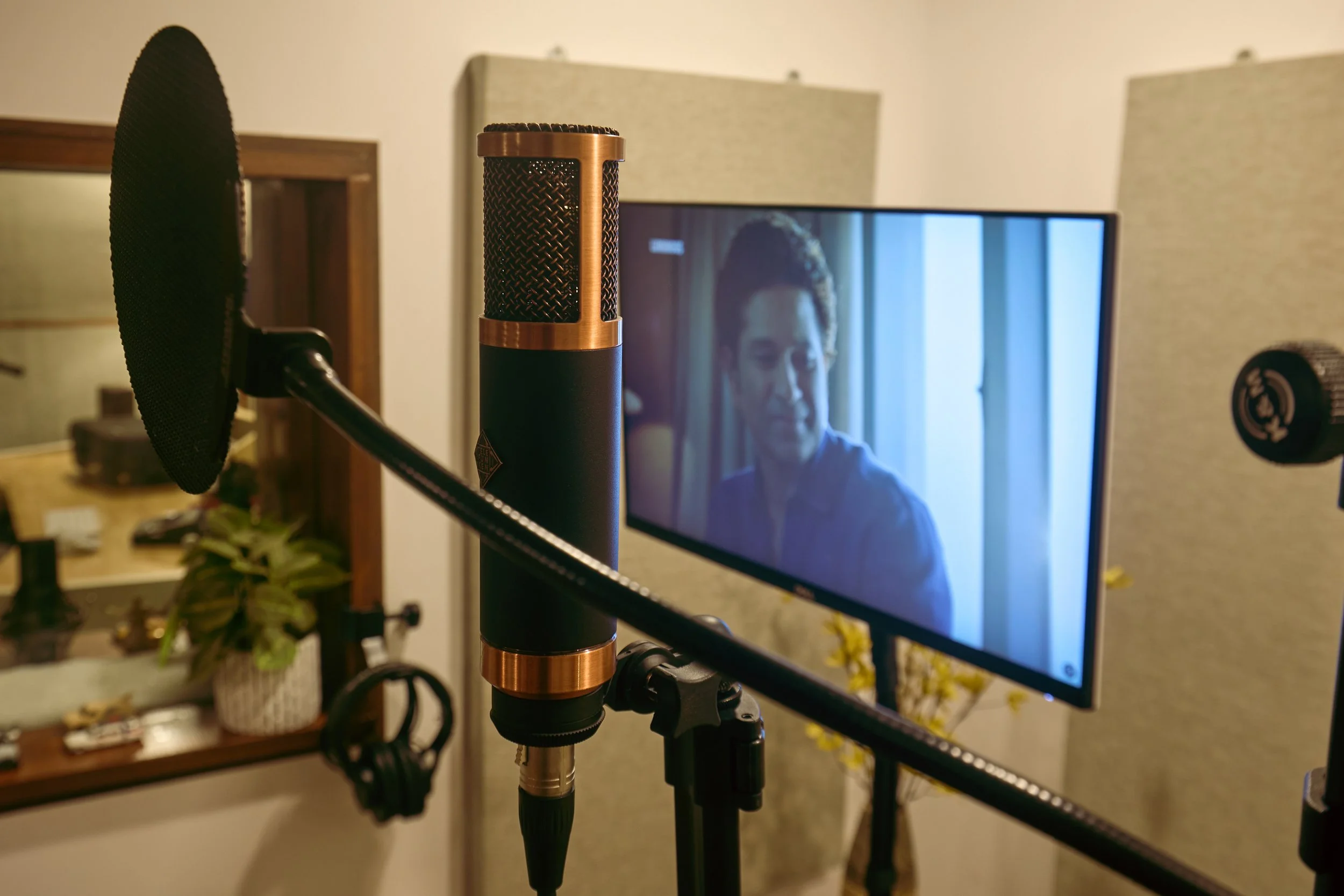 A microphone on a stand in front of a TV screen displaying a man in a blue shirt in a room with beige walls.