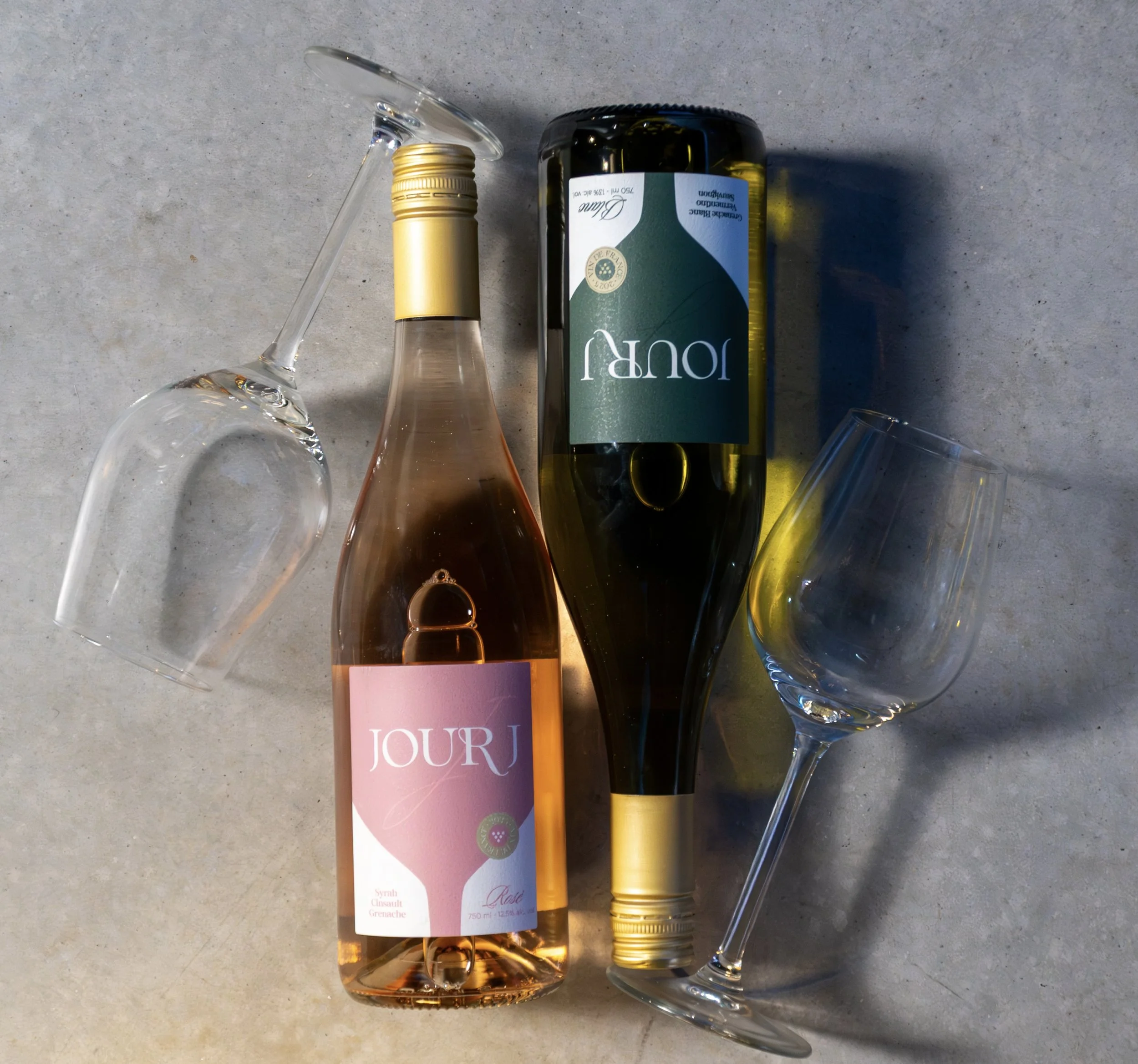A bottle of rosé wine, a champagne flute, an empty glass, and a beer bottle are arranged on a gray surface.