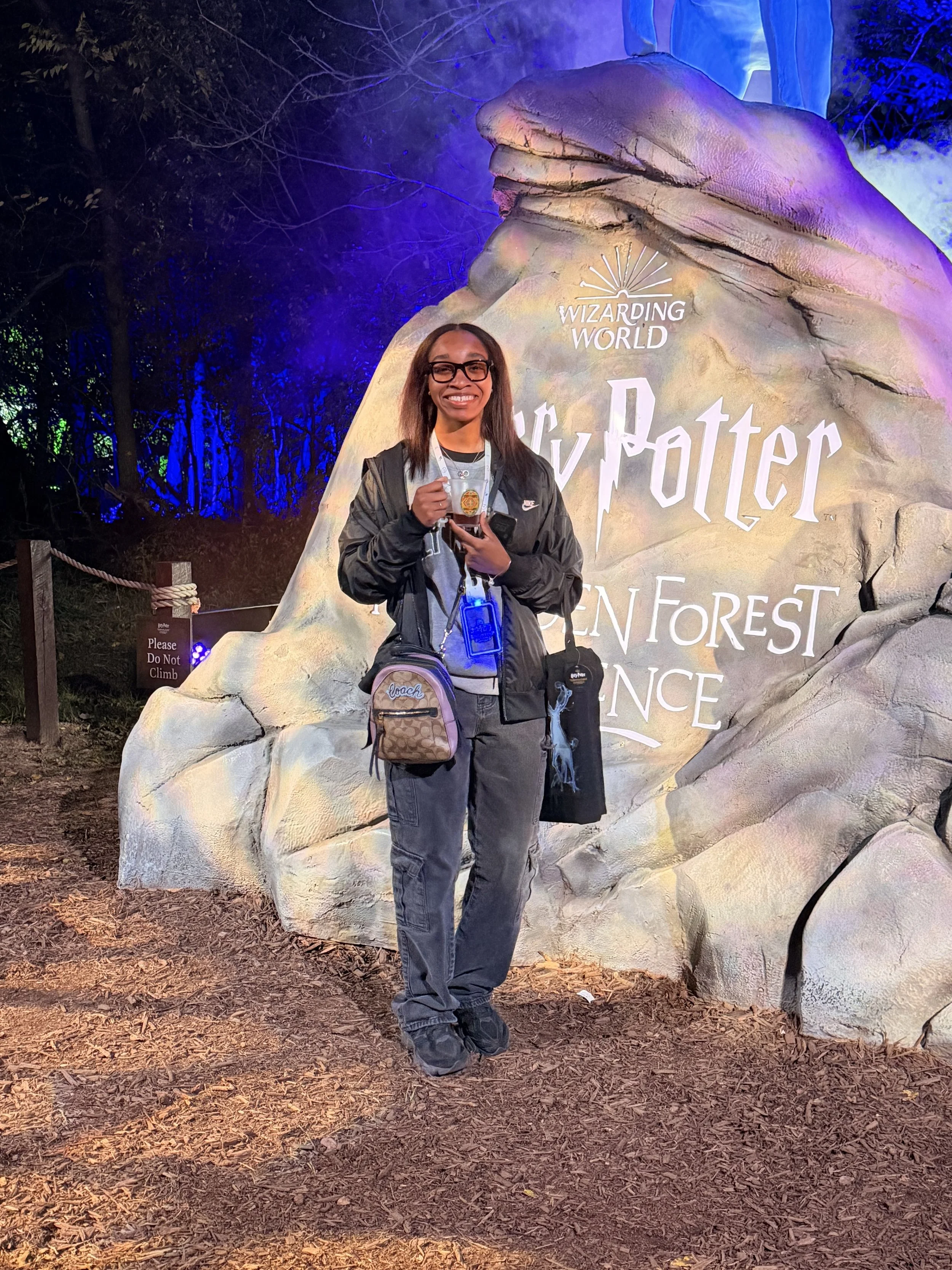 Woman holding a Harry Potter souvenir, standing in front of the Wizarding World sign at Harry Potter theme park.