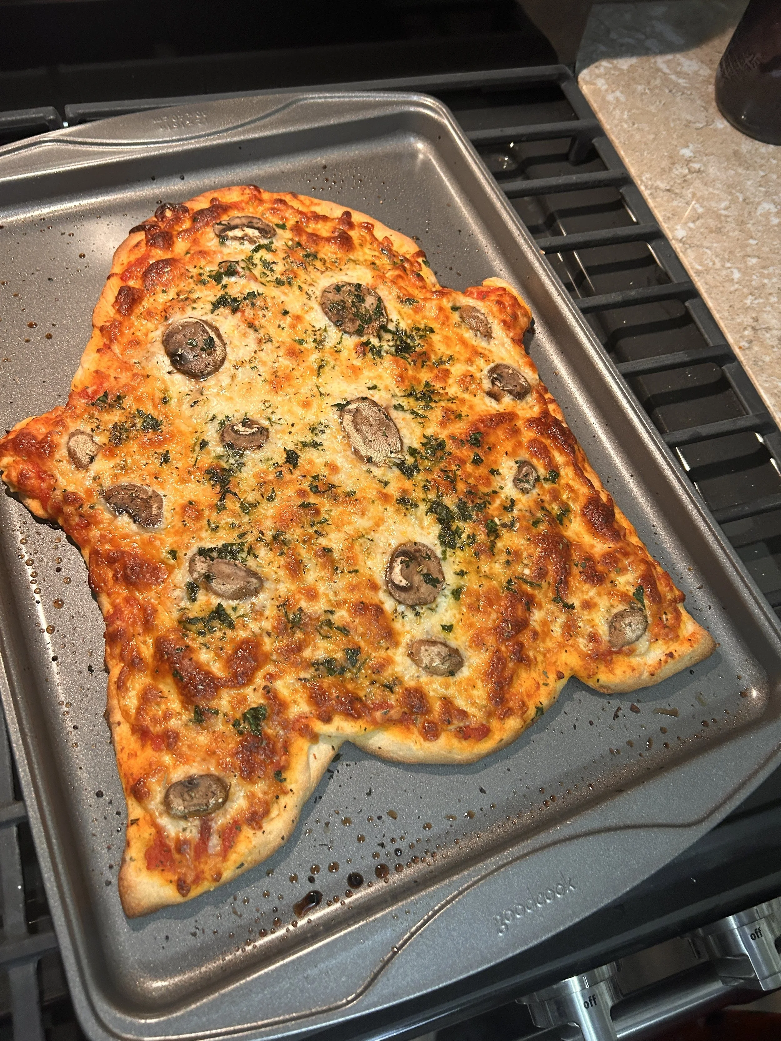 Pizza shaped like a cat with pepperoni and herbs on a baking sheet.