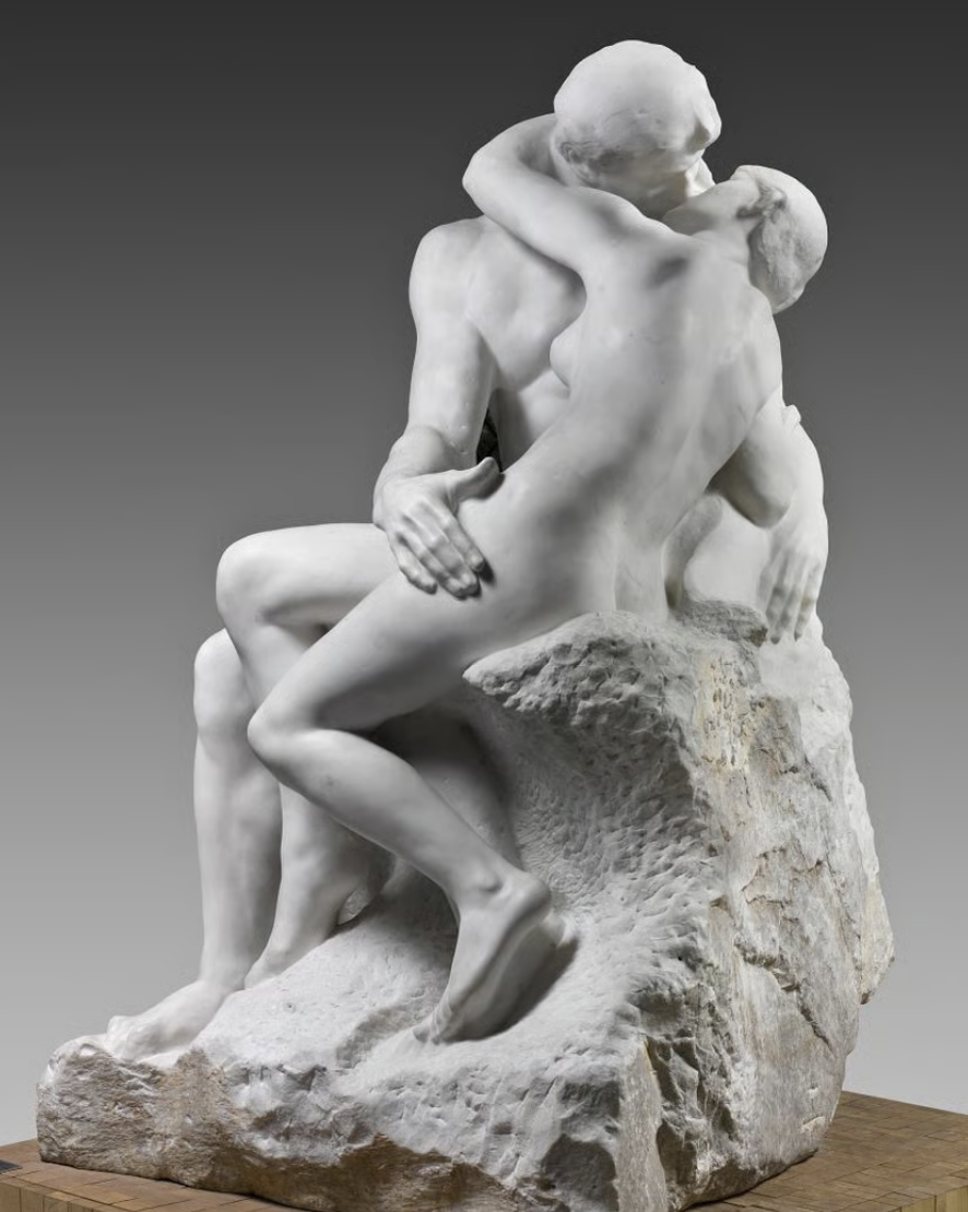 Sculpture de deux personnes en train de s'enlacer, en marbre blanc, avec un fond gris.