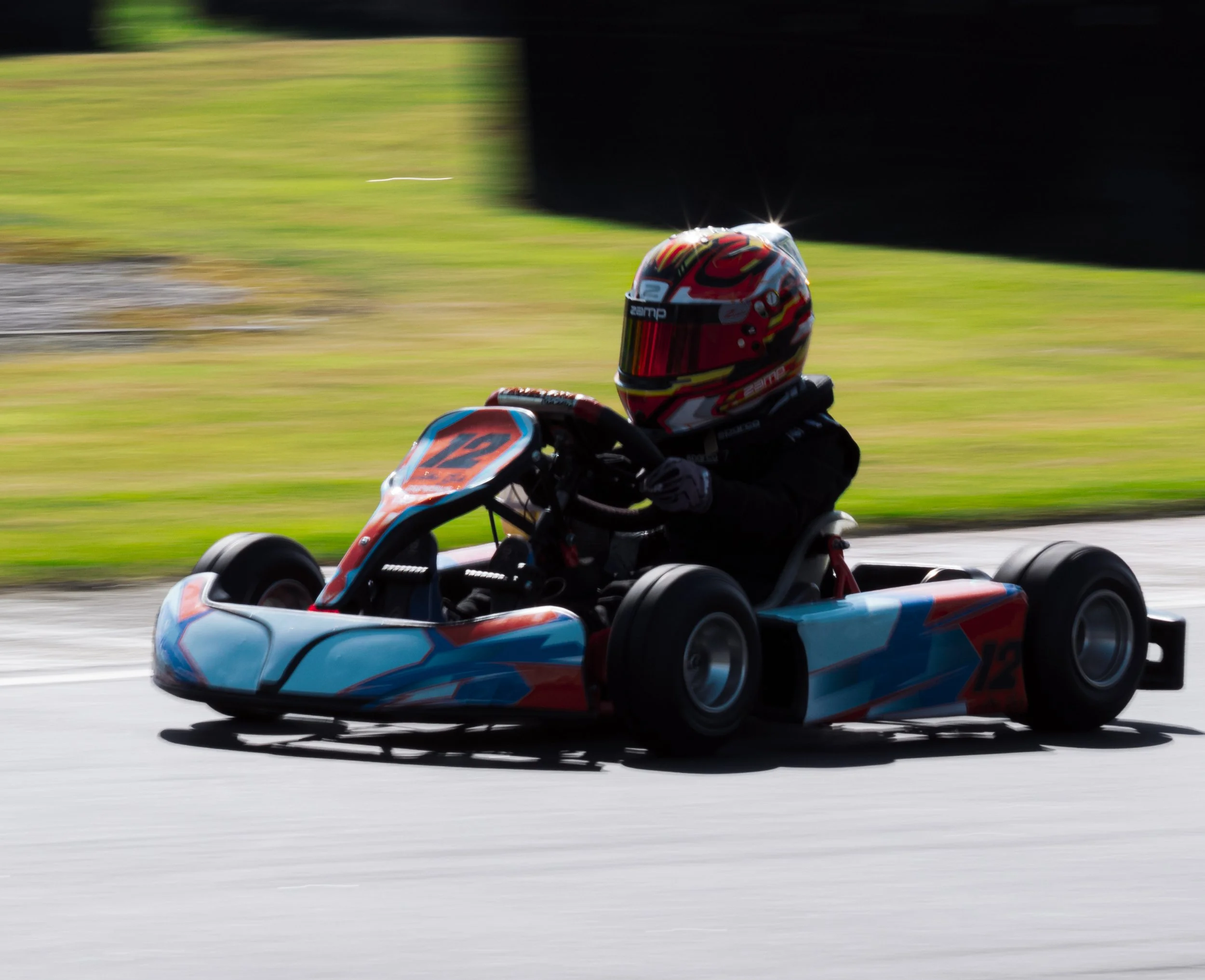 A person racing a go-kart on a track, wearing a helmet and black racing suit.
