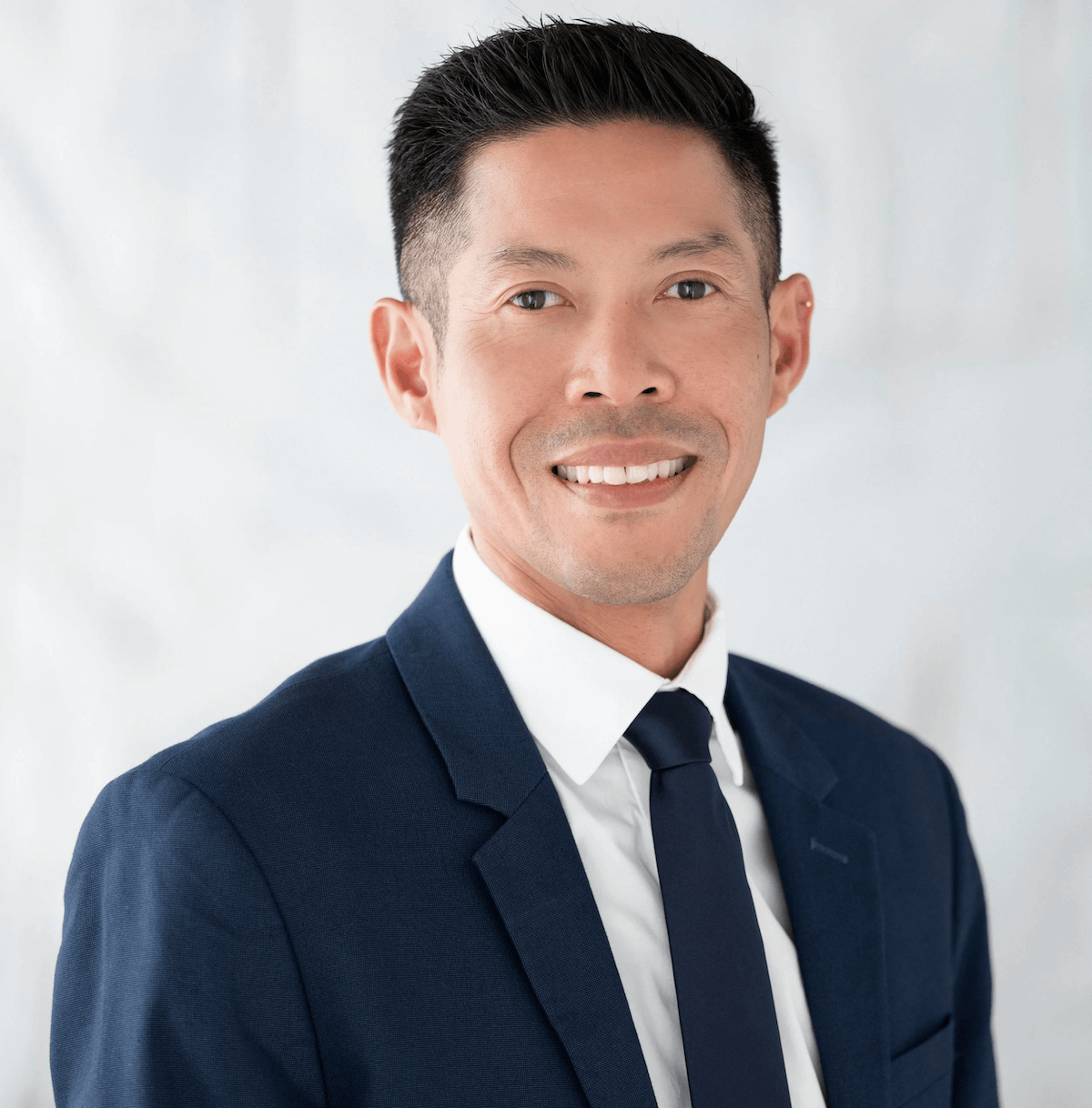 Portrait of a smiling man in a dark suit, white shirt, and dark tie.