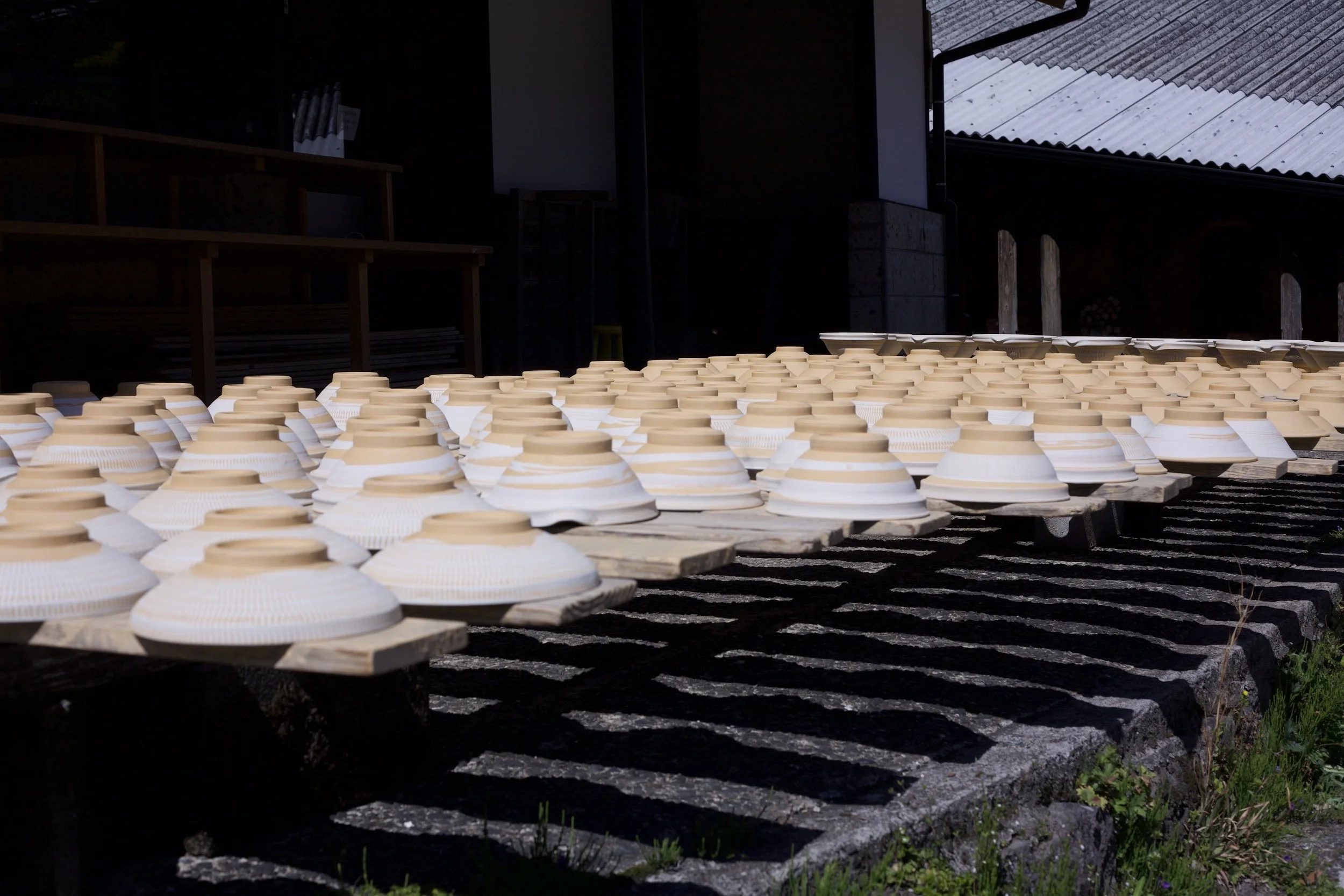 Multiple upside-down bowls drying on wooden planks outdoors at a pottery or ceramic studio in Kyoto.