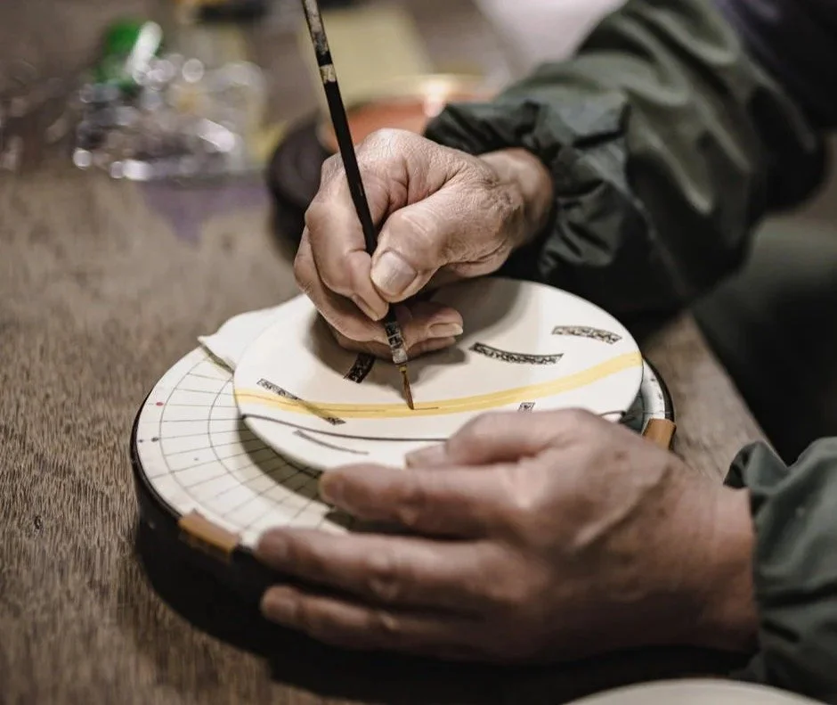 Japanese craftsman drawing Japanese patterns with a thin paintbrush on a porcelain plate in Kyoto.