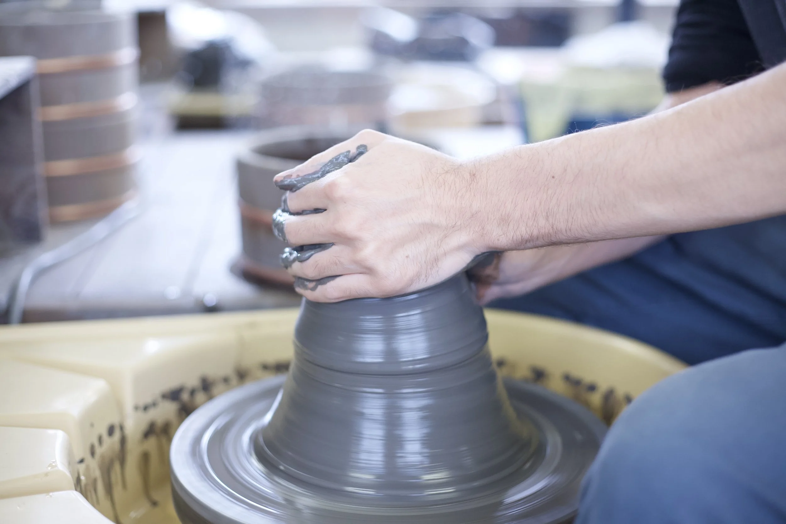 A person shaping a pottery vase on a spinning pottery wheel in a ceramics studio.