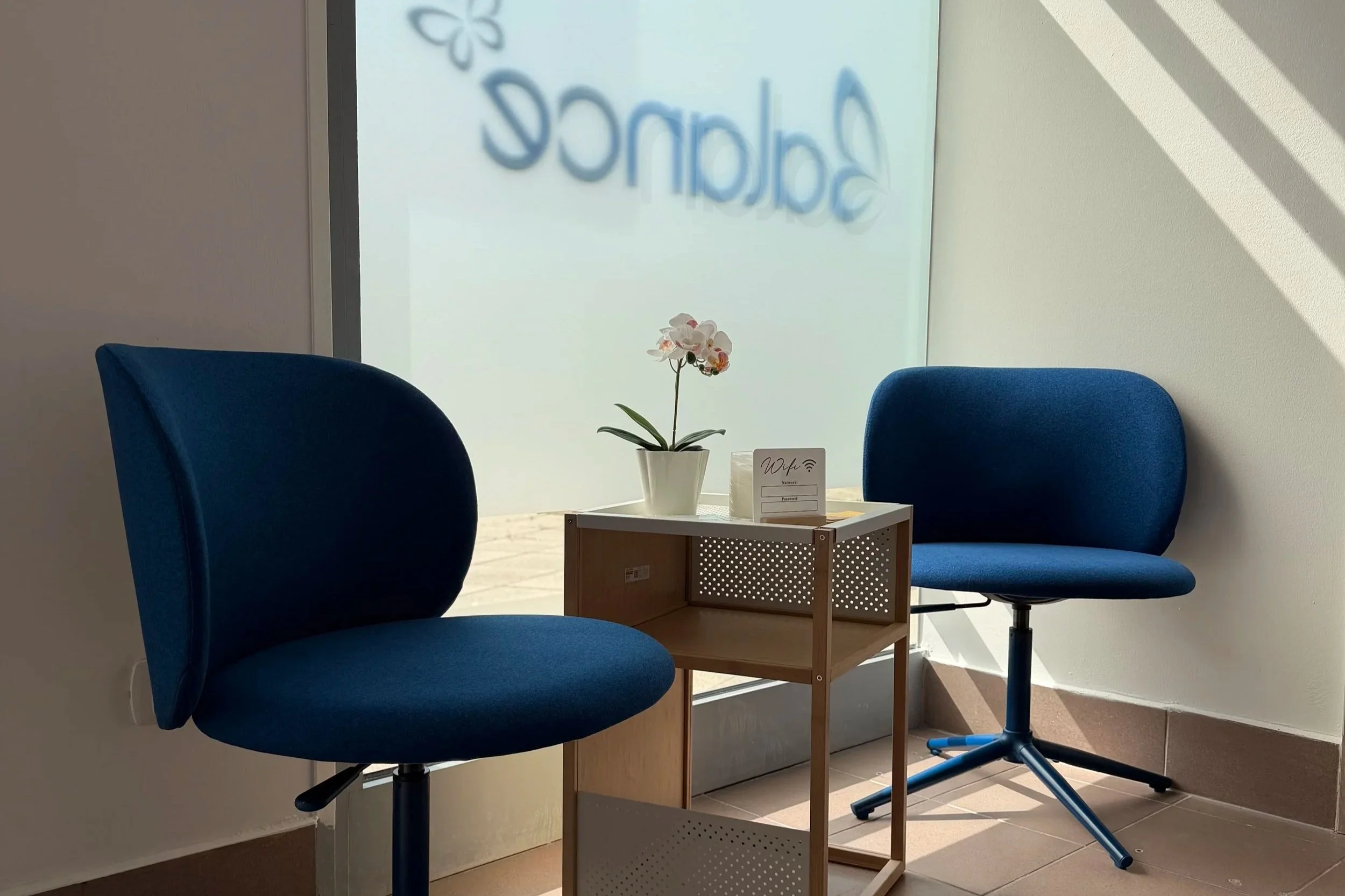 Due sedie blu con schienali curvi di fronte a una finestra con negozio di Calzedonia scritto in blu e un tavolino con una pianta di orchidea bianca e un cartellino Wi-Fi.