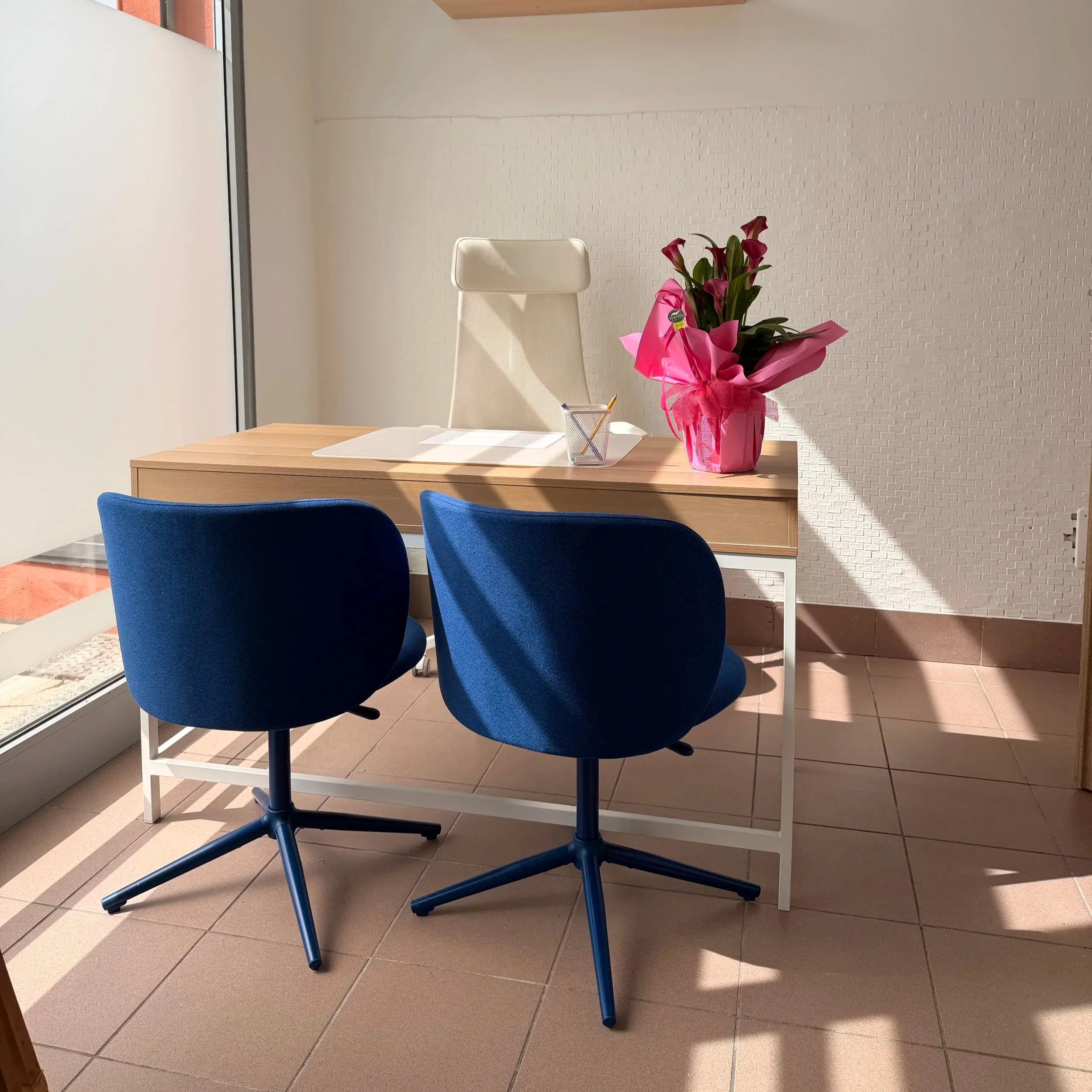 Ufficio con due sedie blu, una scrivania con fiori rosa e una sedia bianca.