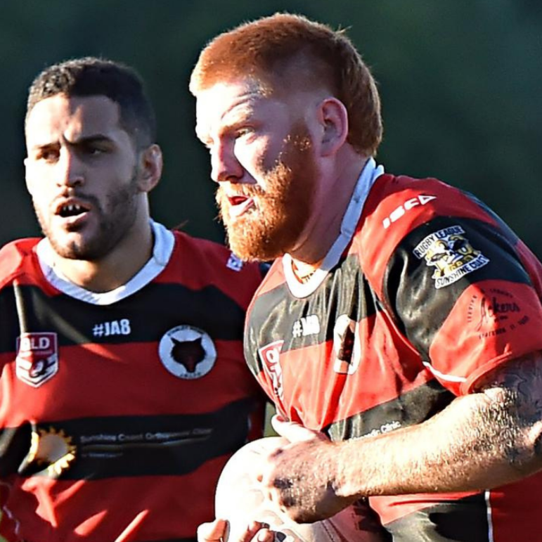Two rugby players in red and black jerseys during a match, one holding a rugby ball, with a blurred green background.