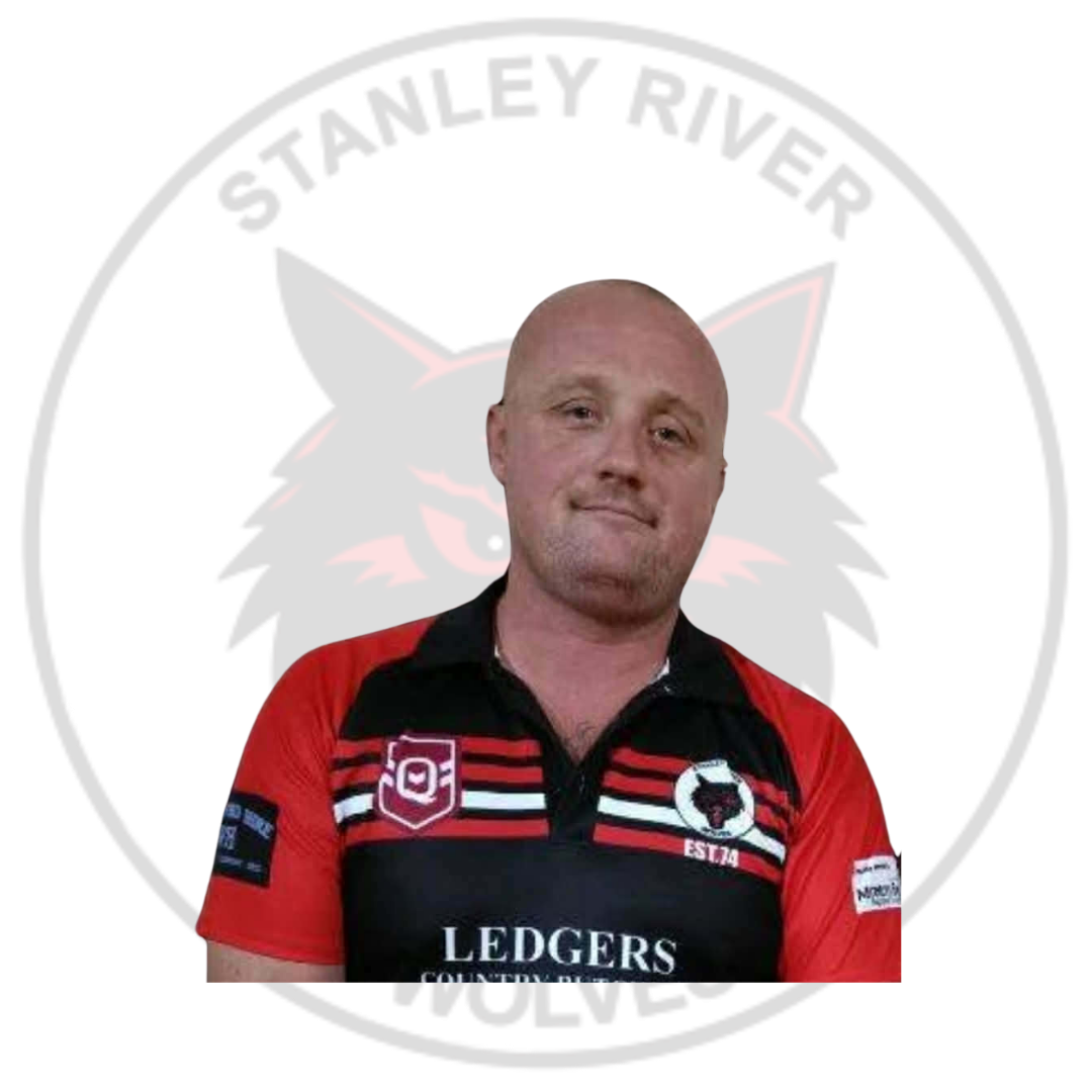 A man with a bald head and light facial hair wearing a red and black sports jersey in front of a circular emblem that reads 'Stanley River Wolves' with a wolf's head logo.