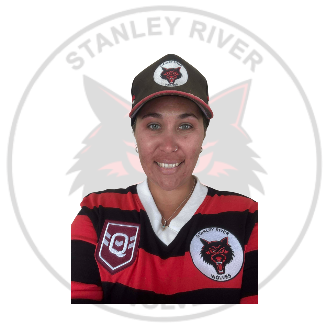 A person taking a selfie in front of a Stanley River Wolves logo. The person is wearing a team jersey and cap with the team's logo, smiling, with short hair, a nose ring, and earrings.