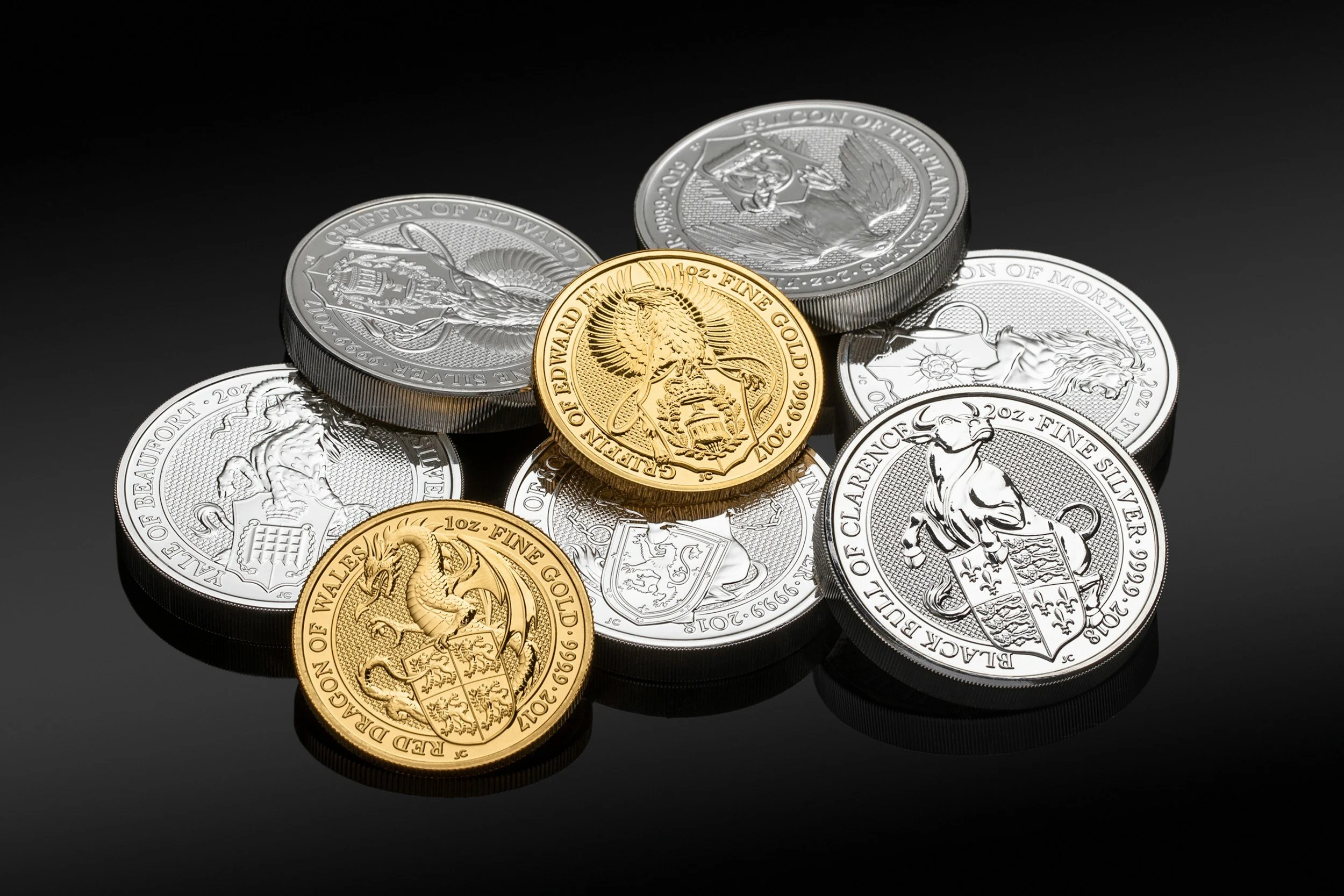 Collection of gold and silver coins on black background, featuring various royal and heraldic designs.