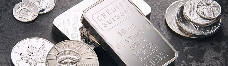 Silver coins and a platinum bar on a dark surface.