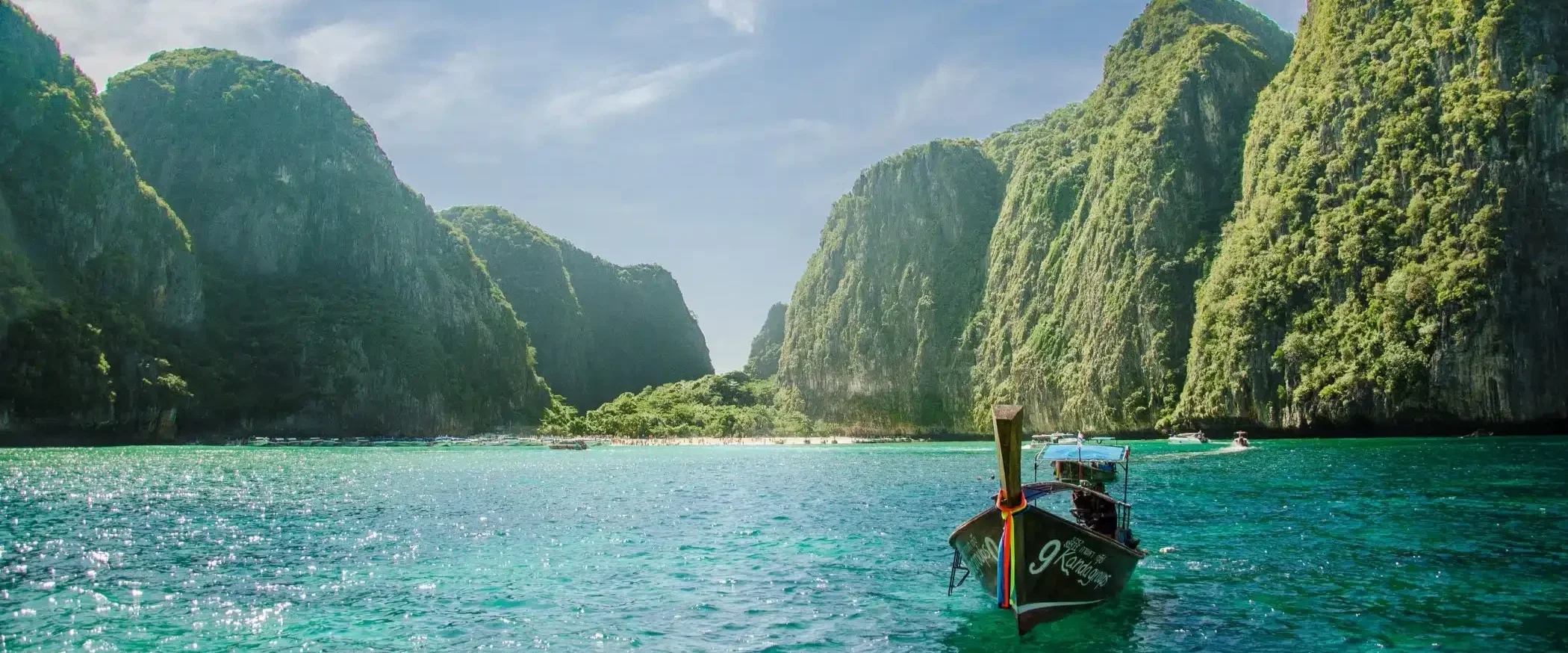 Boat sailing in clear turquoise waters of Phuket with towering green islands and cliffs in the background