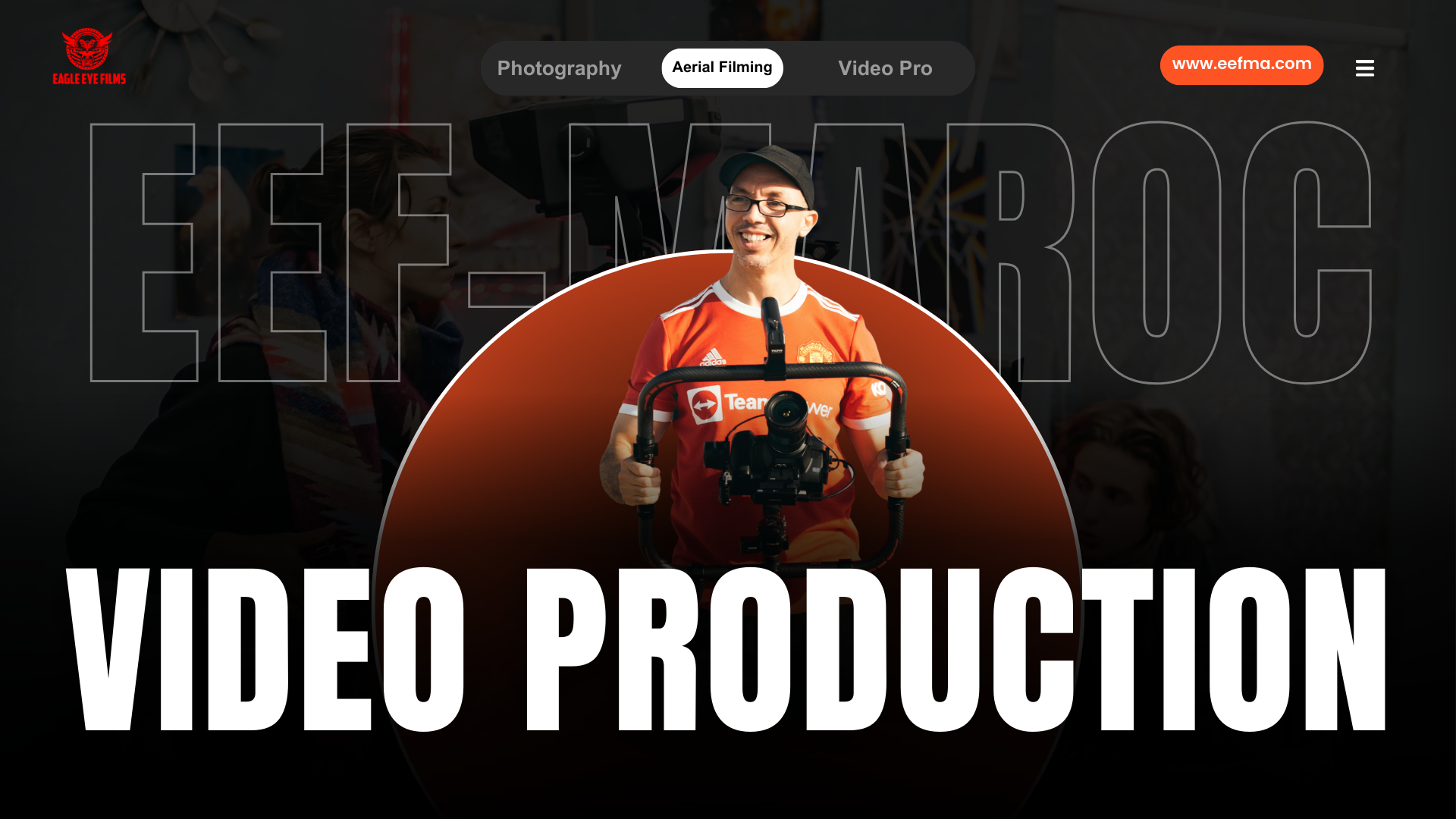 Man holding a professional video camera with a stabilizer, smiling, wearing a red sports jersey and a black cap, in front of a dark background with large text that reads "VIDEO PRODUCTION."