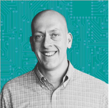 Black and white portrait of a smiling man wearing a checkered shirt in front of a teal background with circuit-like patterns.