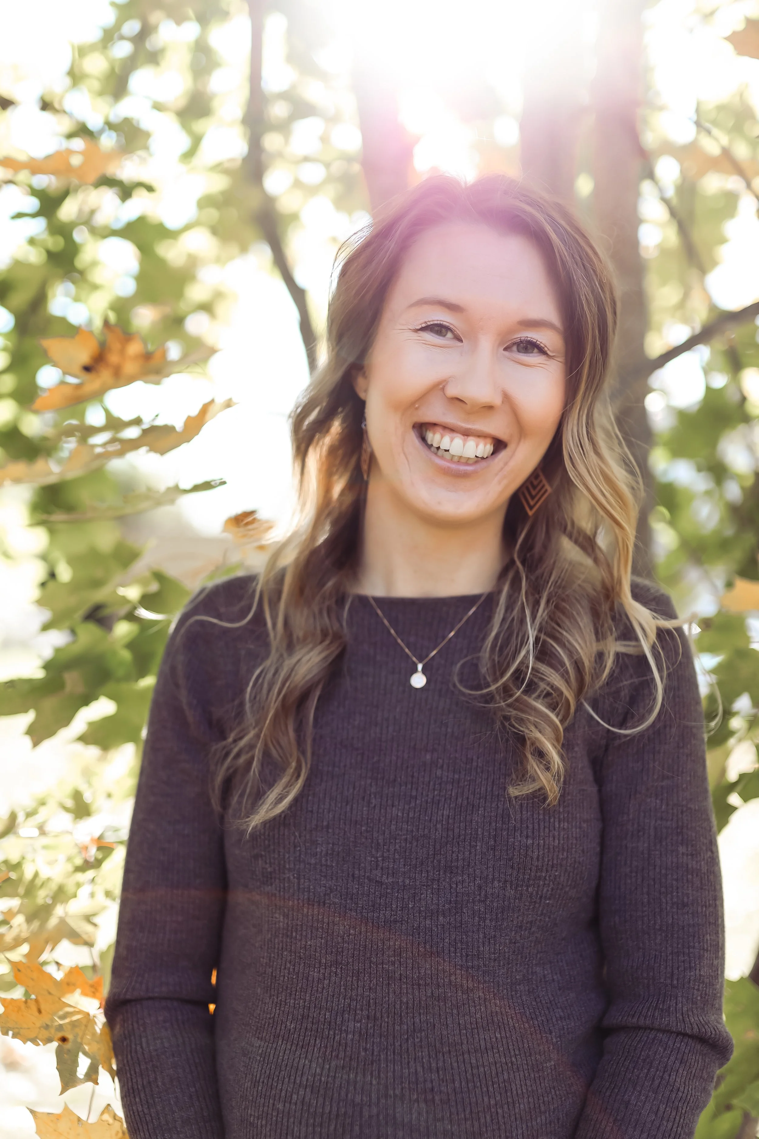 Hymyilevä henkilö syksyisessä puistossa, auringonvalo siivilöityy värikkäiden lehtien läpi ja luo lämpimän tunnelman.