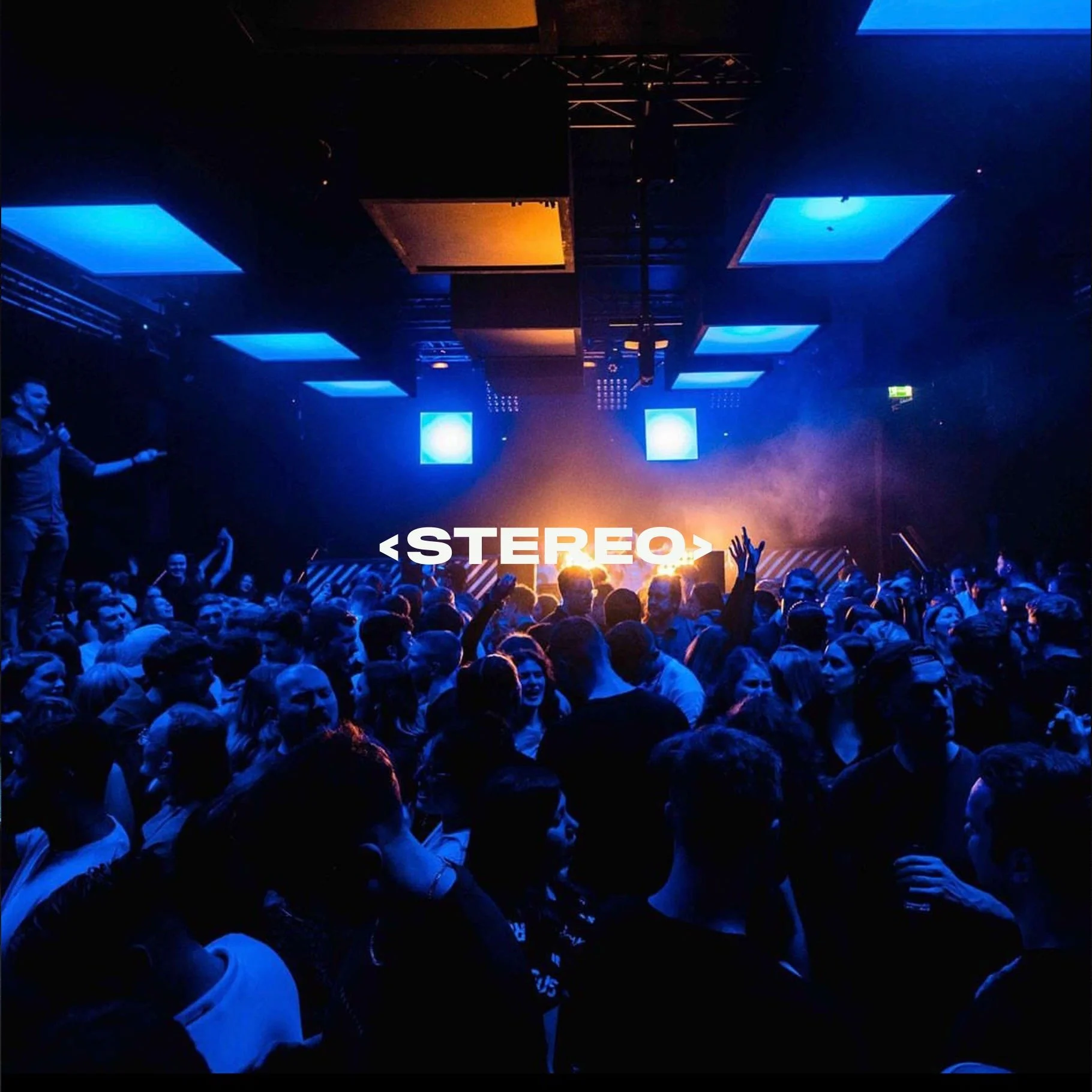 Crowd of people at a concert or nightclub with blue and orange lighting, a DJ or performer on stage, and the word 'STEREO' displayed in large white letters.