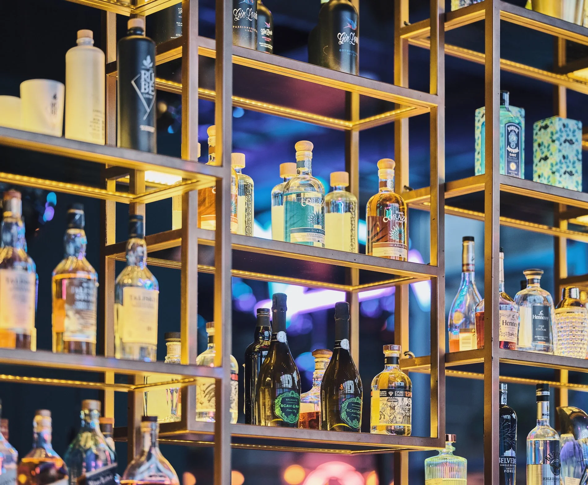 Liv Bar Bielefeld. Bar shelves filled with various bottles of alcohol illuminated by warm lighting.