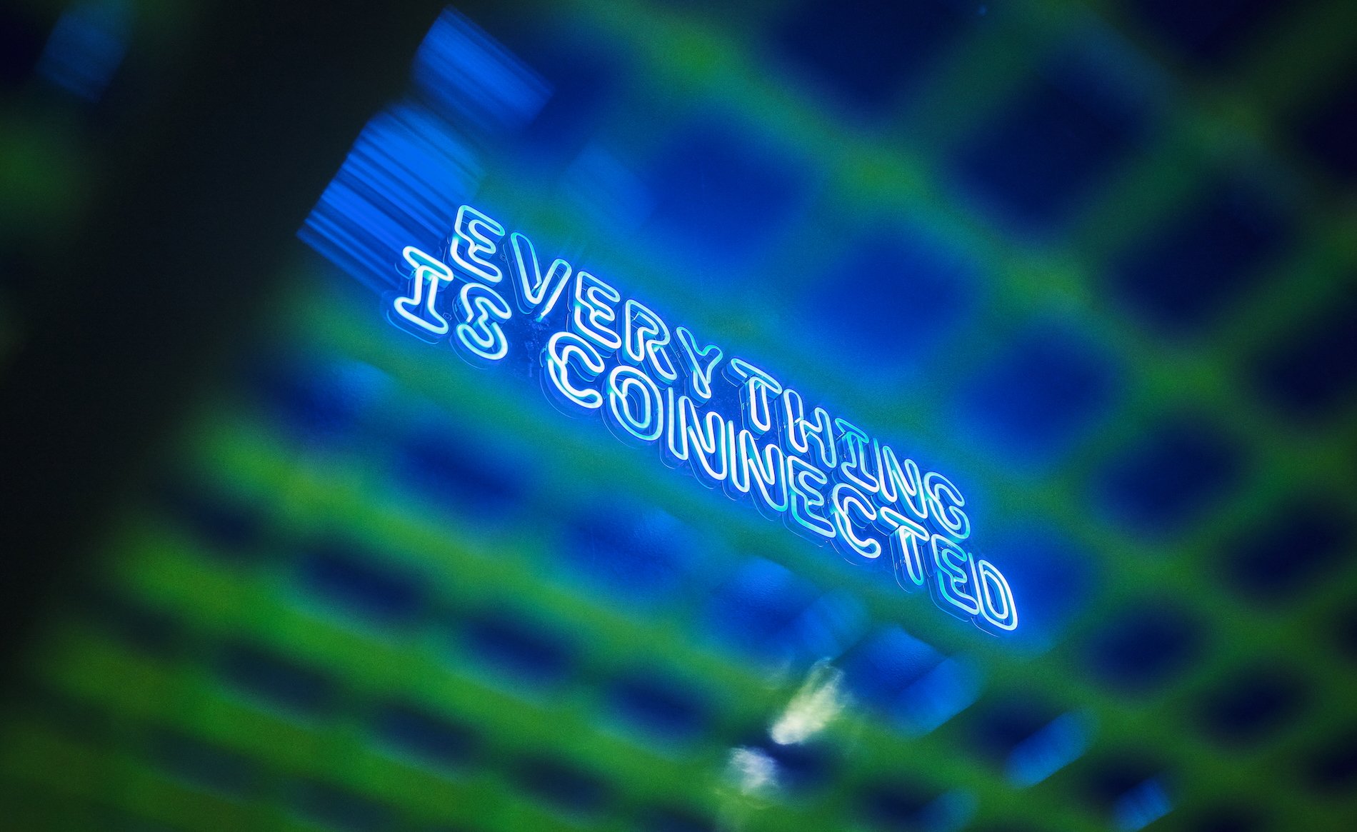 Stereo Bielefeld. Neon sign with blue and green colors that reads 'EVERYTHING IS CONNECTED' with abstract light patterns in the background.
