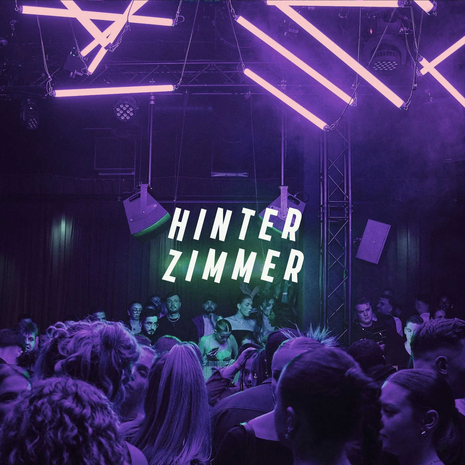 Hinterzimmer Bielefeld. An indoor concert or dance event with a crowd of people illuminated by purple and green lights. There is a large sign displaying the names 'Hinter Zimmer' on a stage backdrop. 
