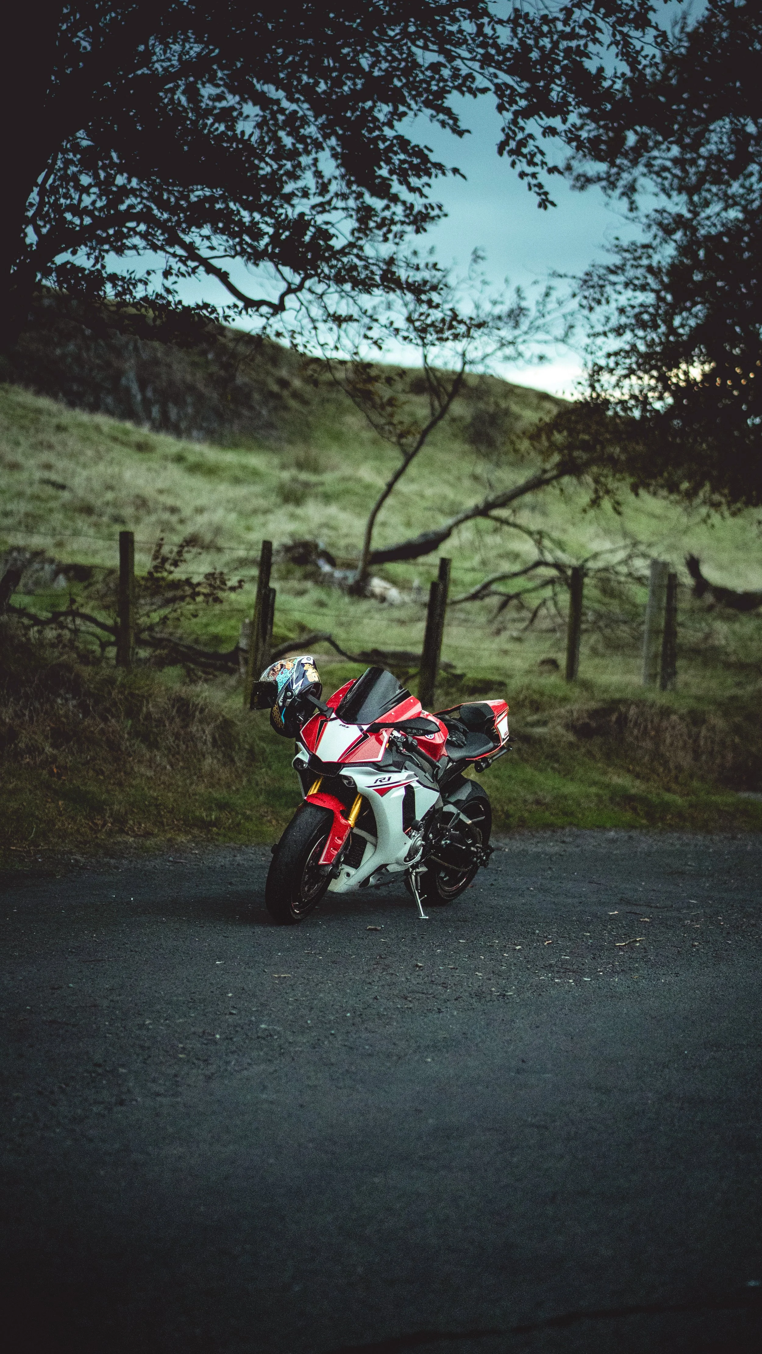 A red and white sport motorcycle parked on a dark road with trees and a fence in the background.