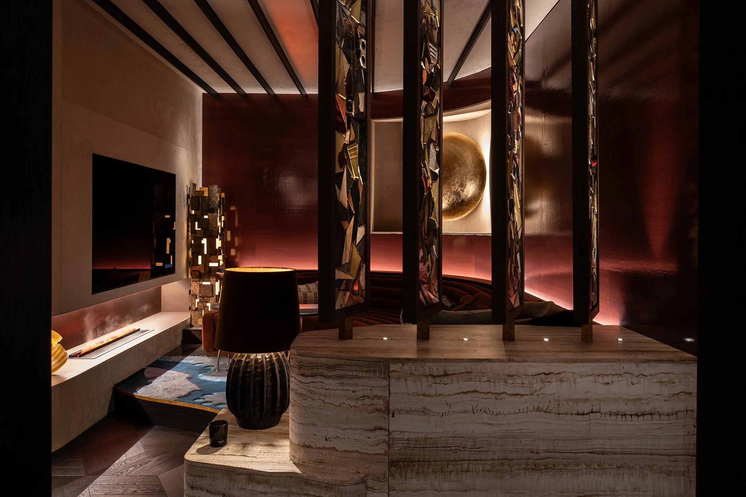 Luxurious interior with dark wood and marble accents, a large round gold art piece on the wall, and a mosaic partition. Warm lighting creates a cozy atmosphere.