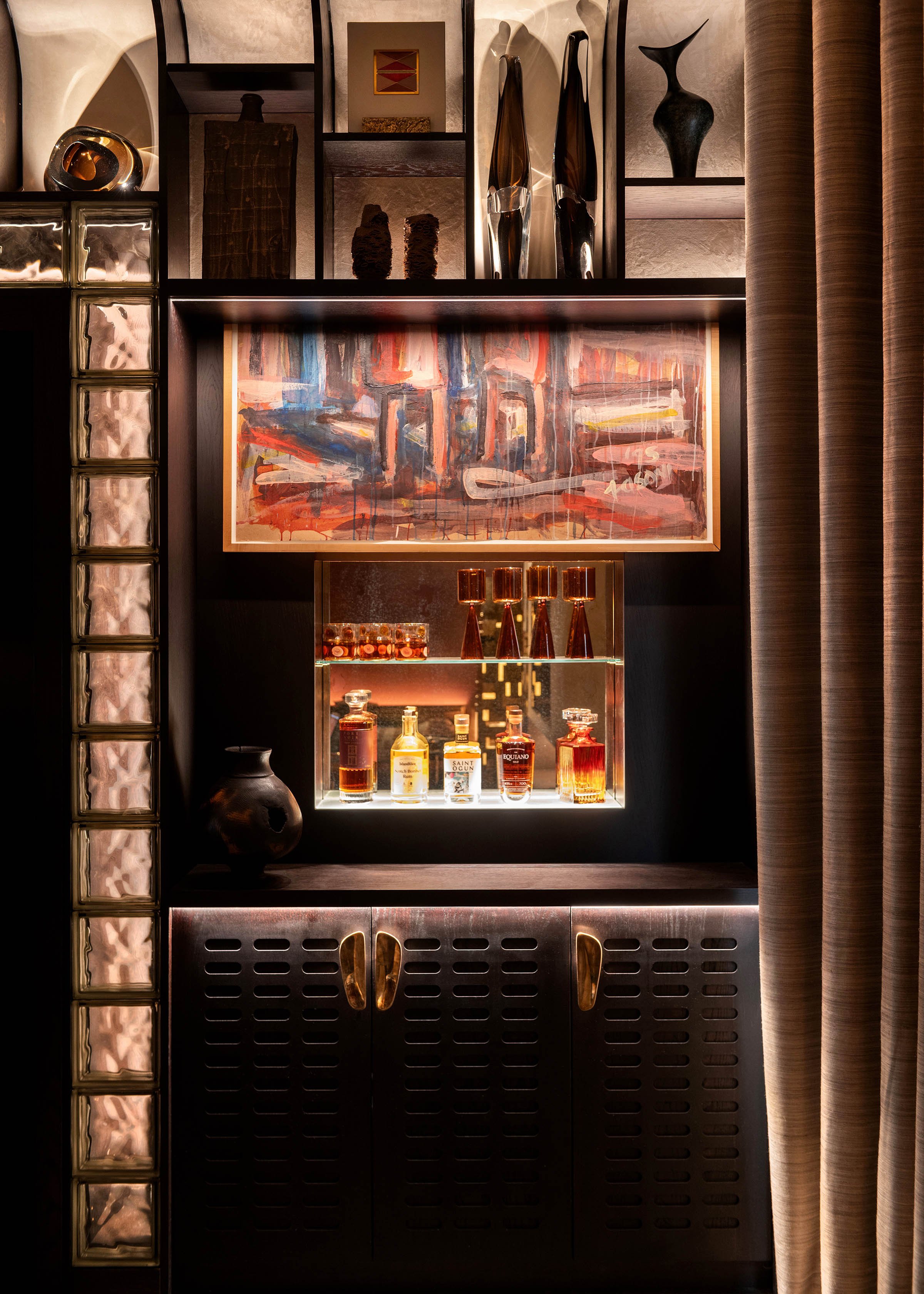 A stylish bar cabinet with glass bottles, decorative vases, colorful abstract painting, and decorative objects, illuminated with warm lighting.