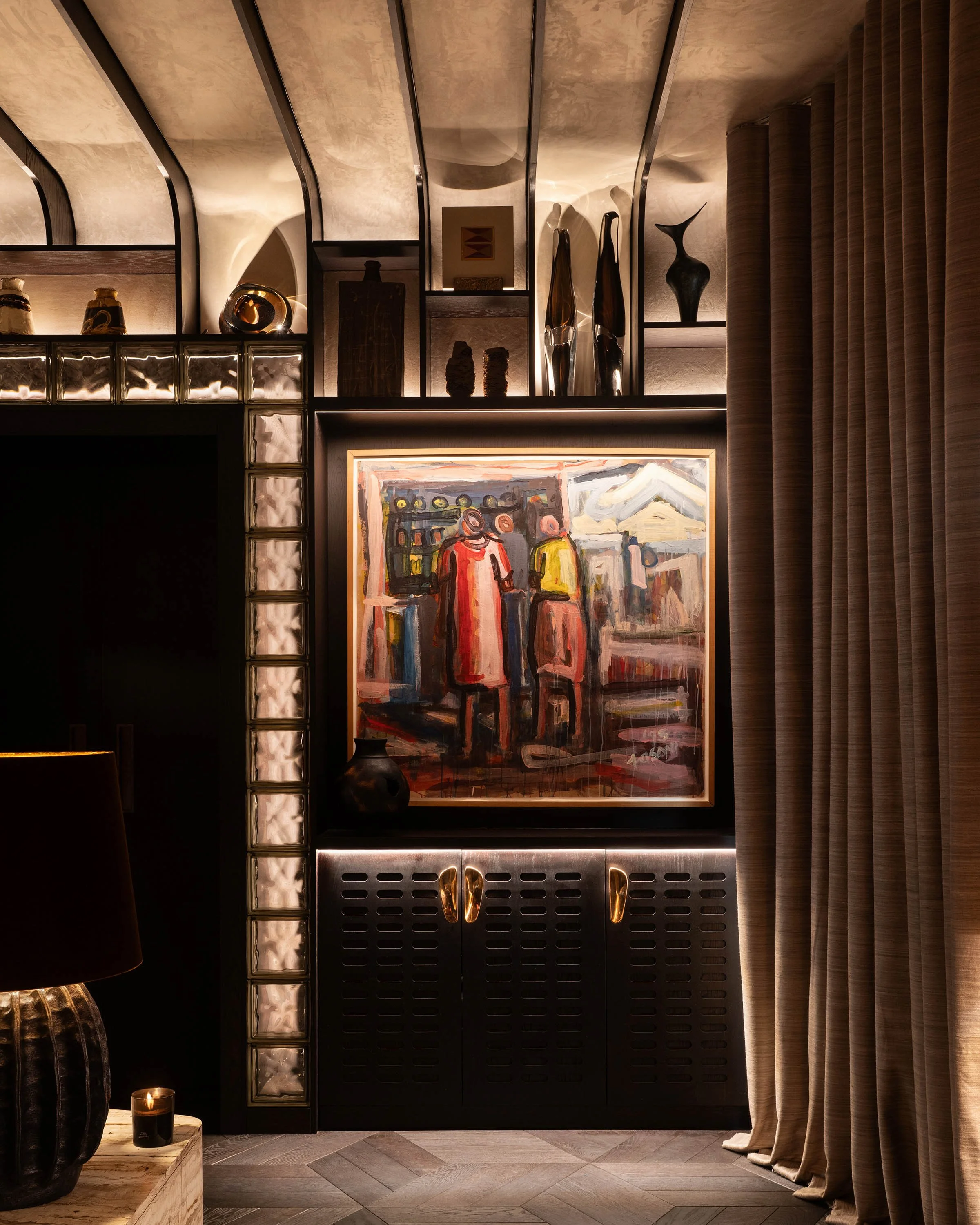 A modern living room corner with dark cabinetry, a colorful abstract painting, decorative vases, and a curved, textured curtain.