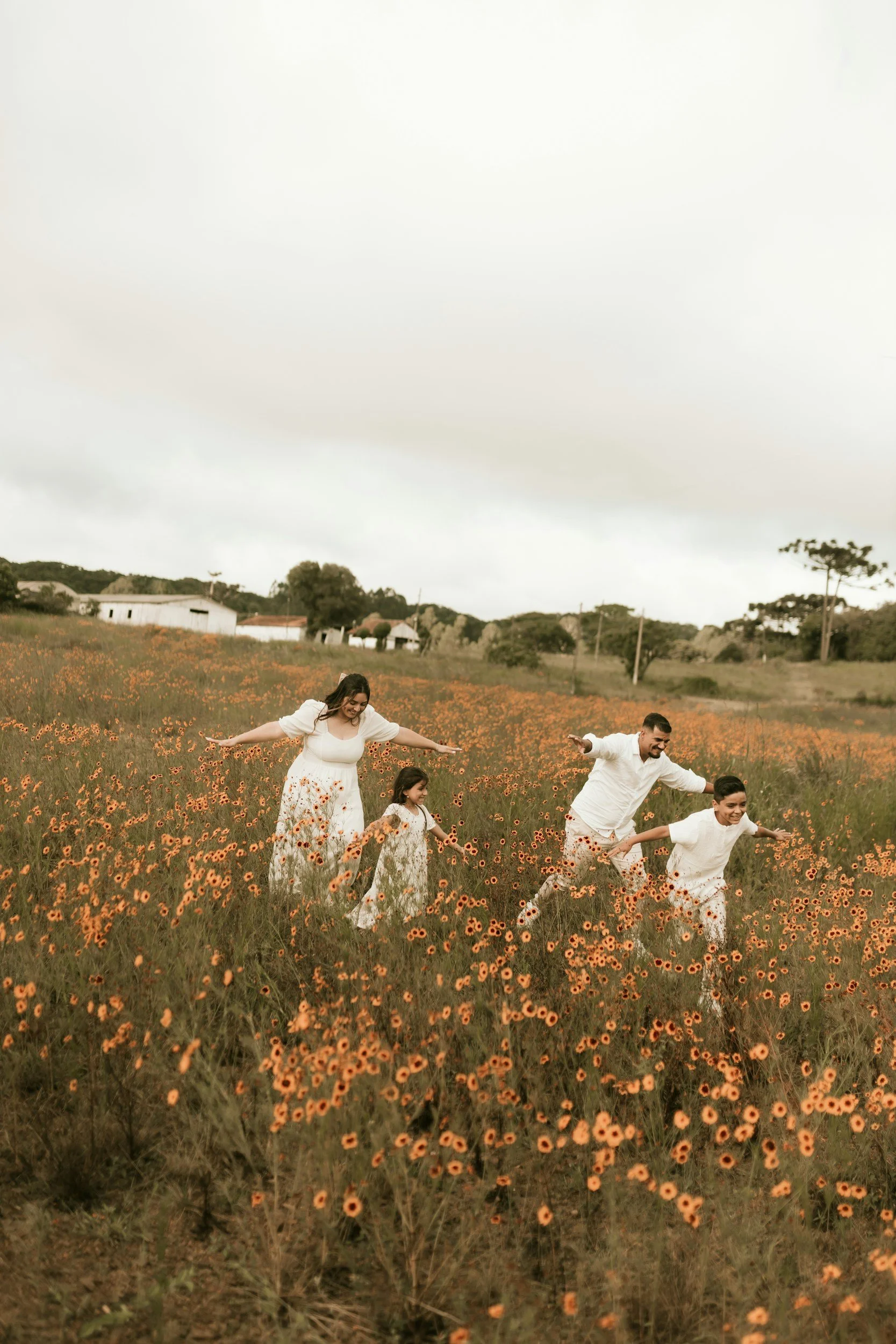 A family of four, dressed in white, enjoying a walk through a field of orange flowers on a cloudy day.