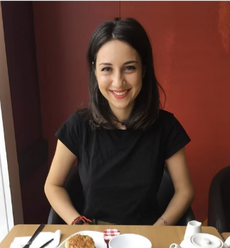 A young woman with black hair smiling while sitting at a table in a dining setting.