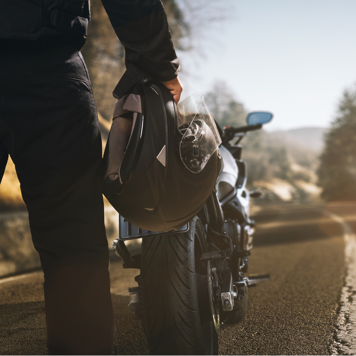 Person holding a motorcycle helmet next to a black motorcycle on a mountain road.