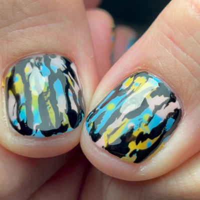 Close-up of two fingernails with colorful abstract nail art, featuring black, yellow, blue, white, and gray streaks.
