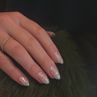A hand with manicured nails resting on a dark furry surface, wearing a gold ring on the ring finger.